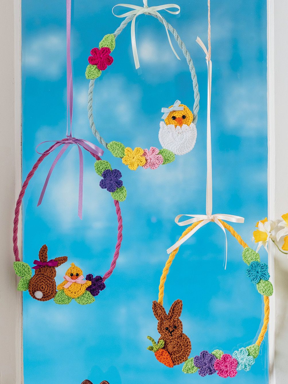 Handgemachte, bunte Häkel-Ostereier und -hasen mit Blumen und Schleifen. Perfekt für DIY-Liebhaber.