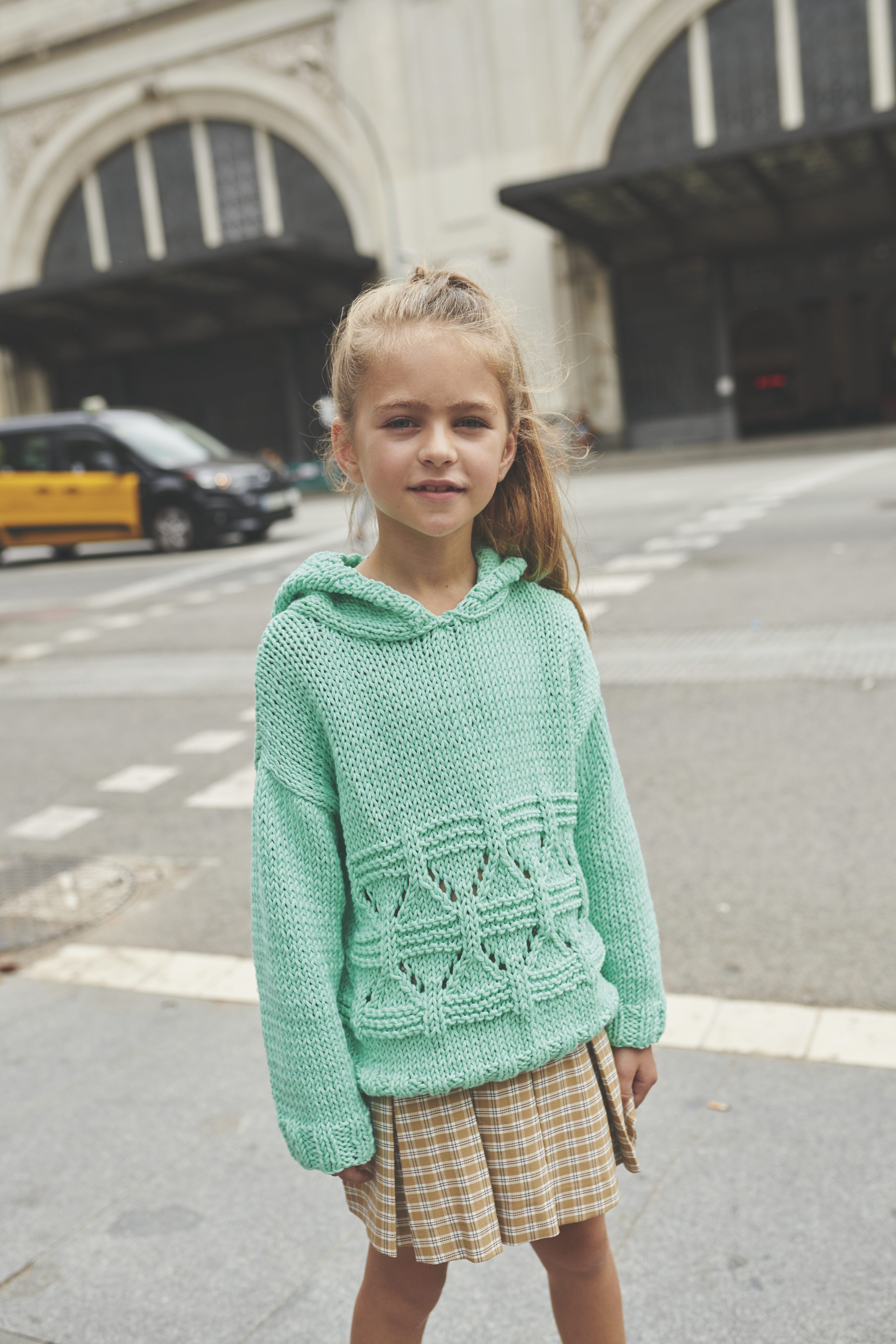 Mintgrüner, handgestrickter Pullover mit Lochmuster; karierter Rock; modisch, mit handgemachtem Flair.