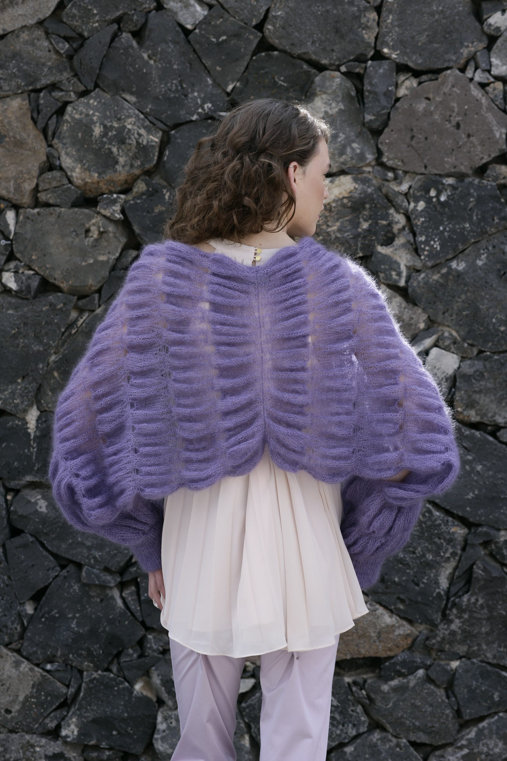 Modisches DIY-Lila-Strickoberteil mit luftigen, handgemachten Mustern über cremefarbener Kleidung.