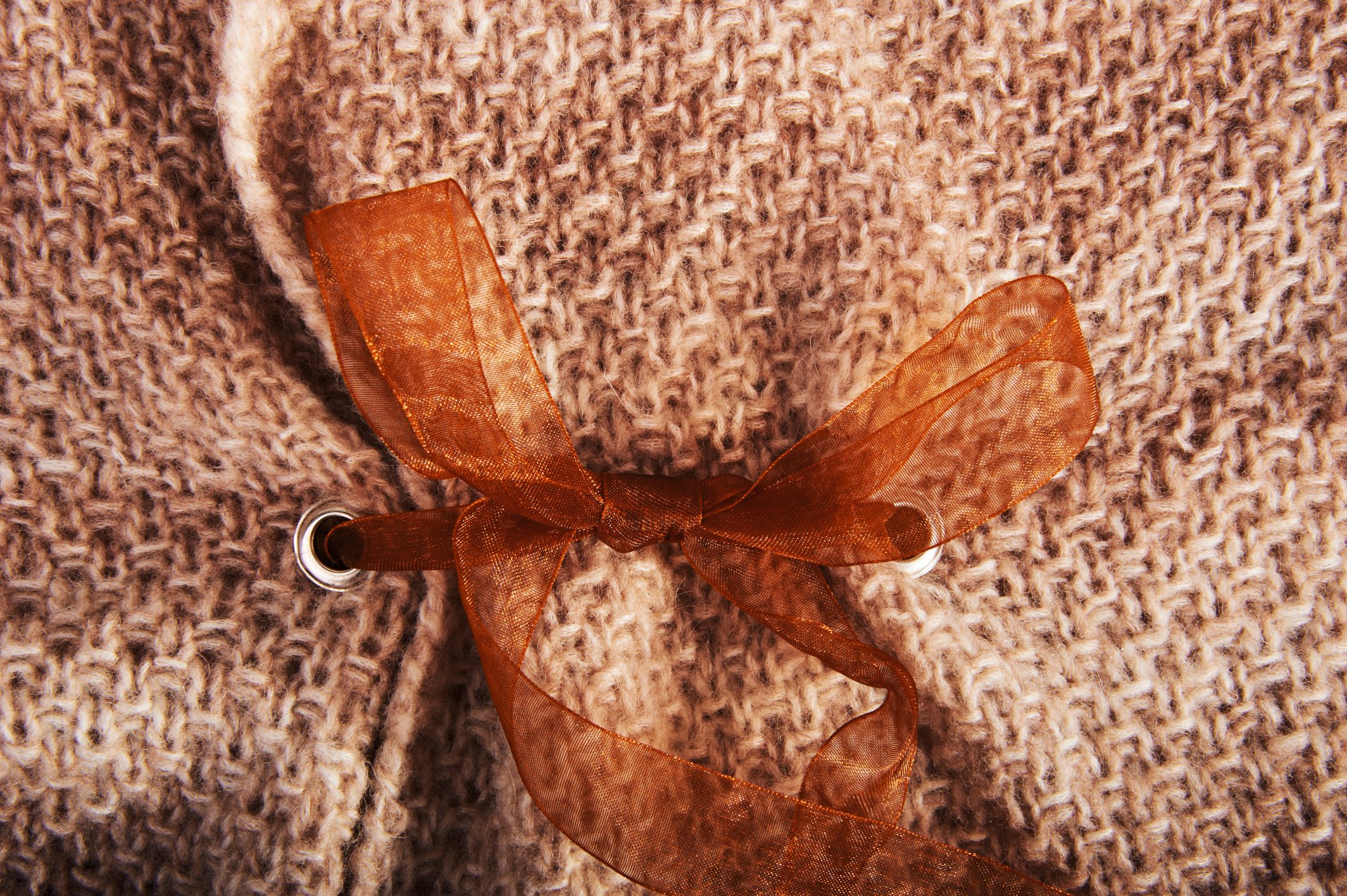 Beigefarbenes Strickmuster mit brauner Schleife. Handgefertigtes, modisches Detail.