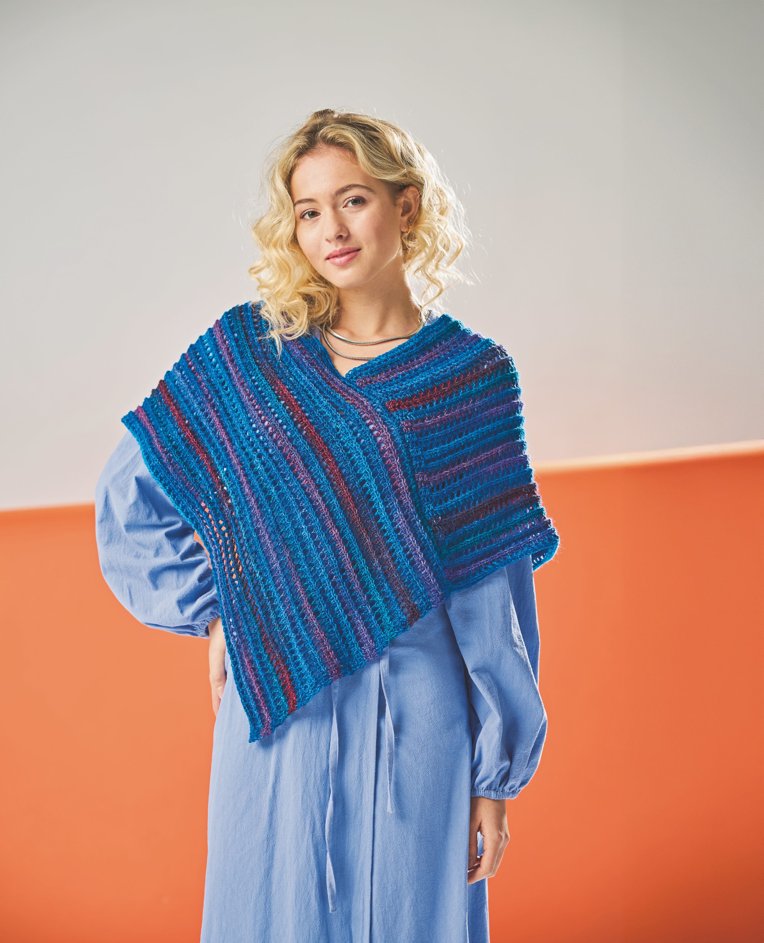 Handgemachter, bunter Strickponcho in Blau und Violett über weitem, hellblauen Kleid. Modisch und einzigartig.