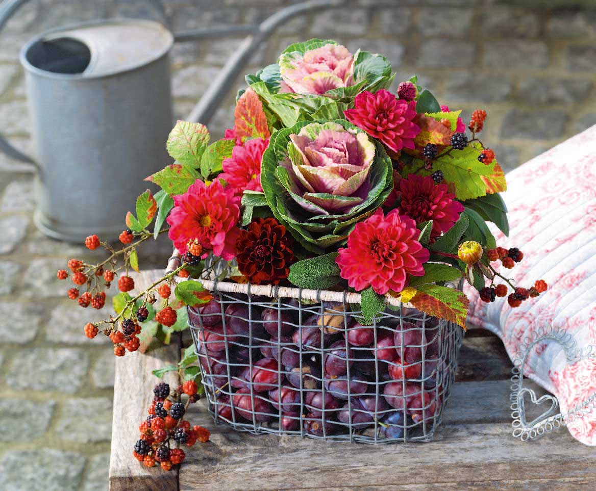 Drahtkorb mit selbstgemachten Blumenarrangement in kräftigem Rot und Grün, ergänzt durch Beeren.