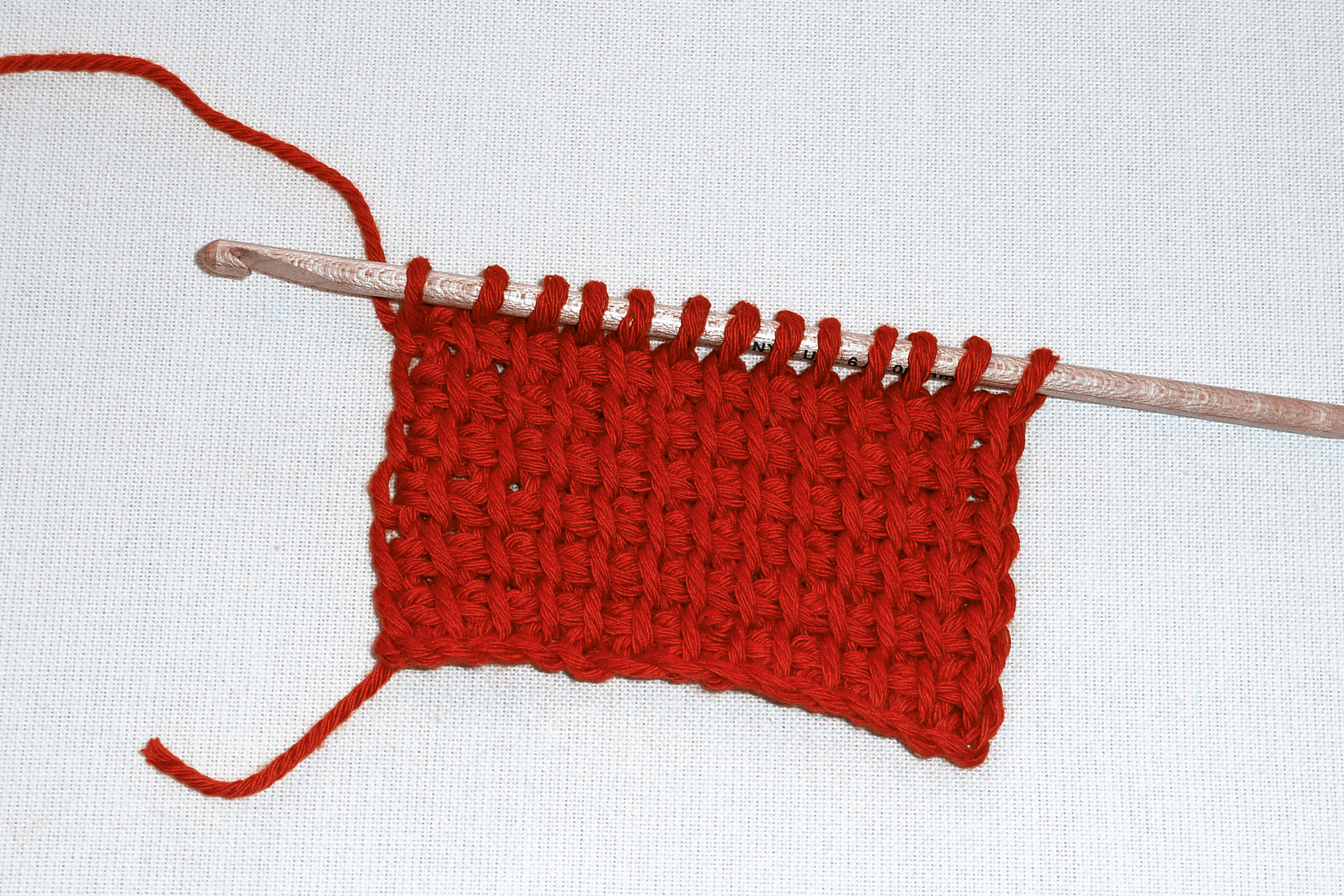 Tiefrote Maschen kunstvoll an Häkelnadel. Modisches, handgemachtes DIY-Strickstück. Feine Webstruktur.