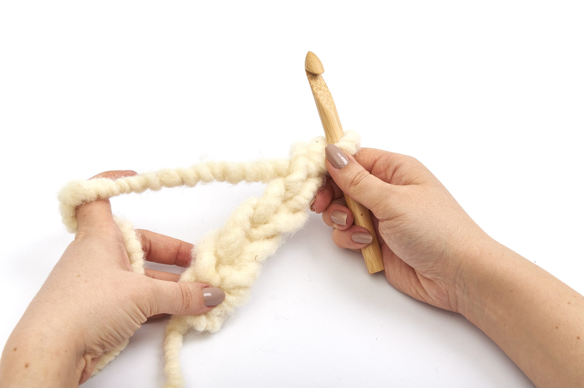 Große Häkelnadel mit cremefarbener, flauschiger Wolle. DIY, selbstgemacht, Handwerk.