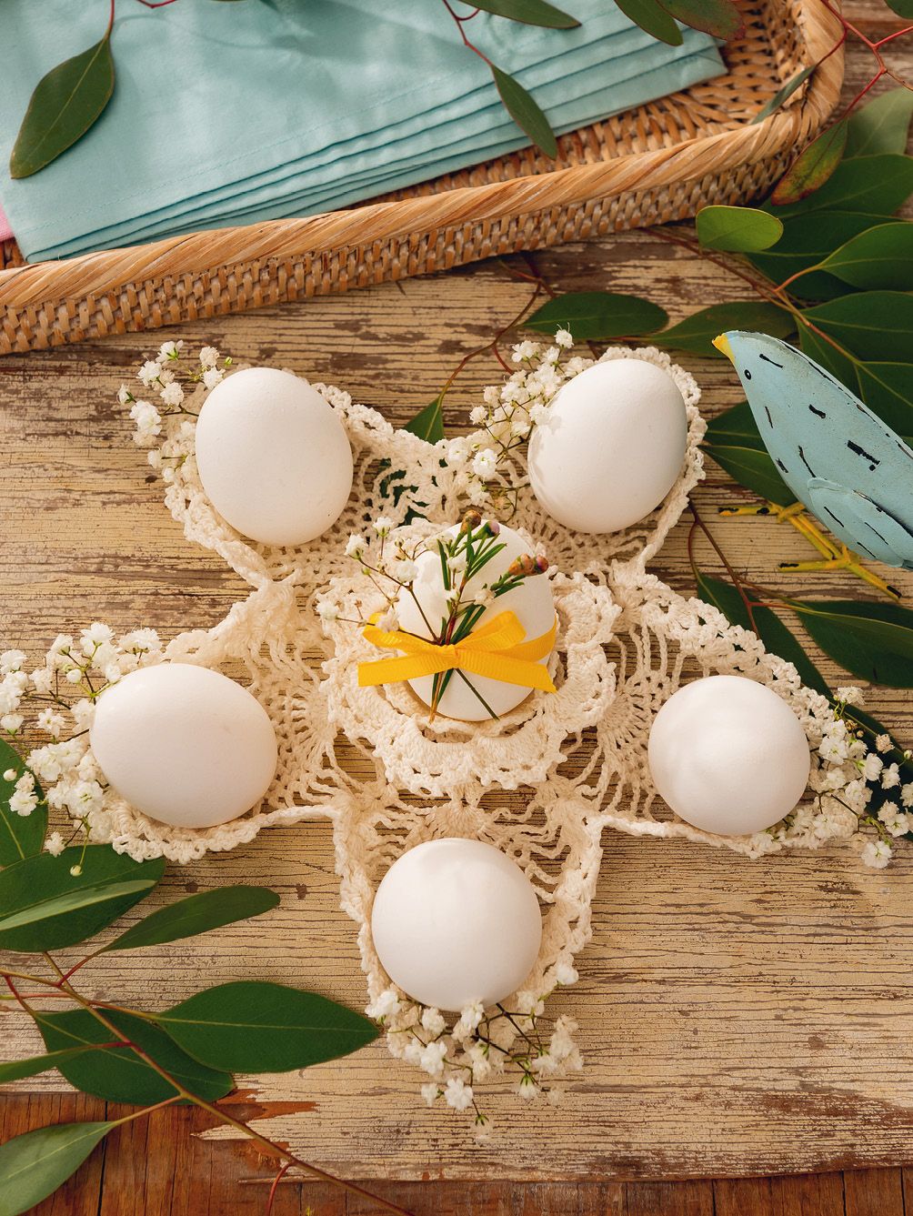 Weiße Eier auf handgearbeitetem Häkeldeckchen, verziert mit gelber Schleife und zarten Blumen; DIY Ostertisch.