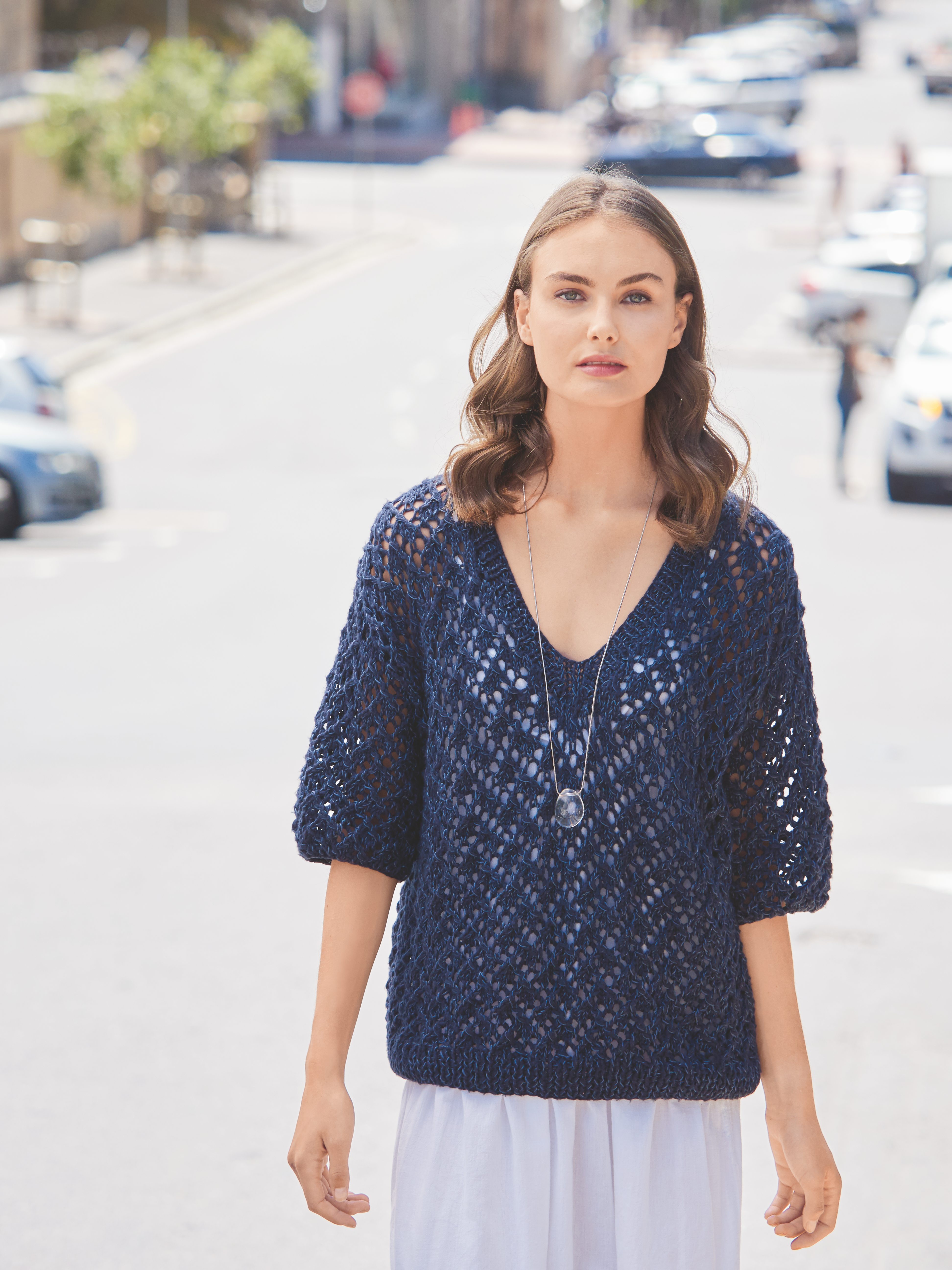 Modischer blauer Strickpullover, grobmaschig, mit V-Ausschnitt. Kombiniert mit luftiger, weißer Bekleidung.