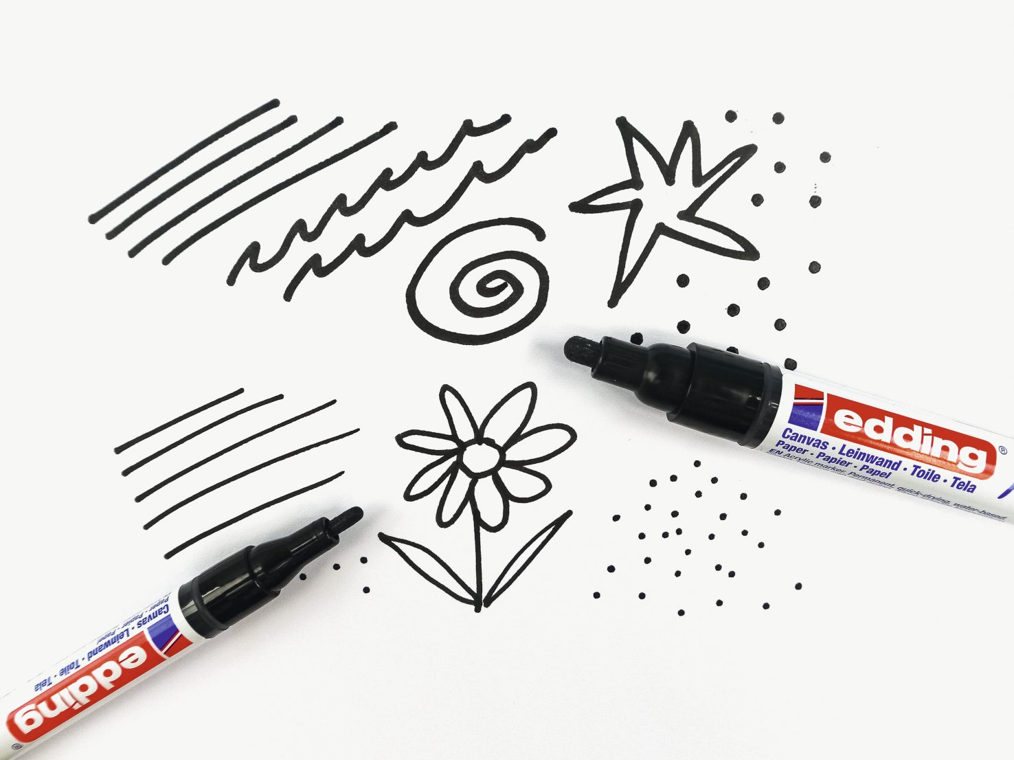 Schwarze Filzstifte auf Papier mit handgemachten Mustern: Linien, Spiralen, Stern, Blume. Modisch, DIY.