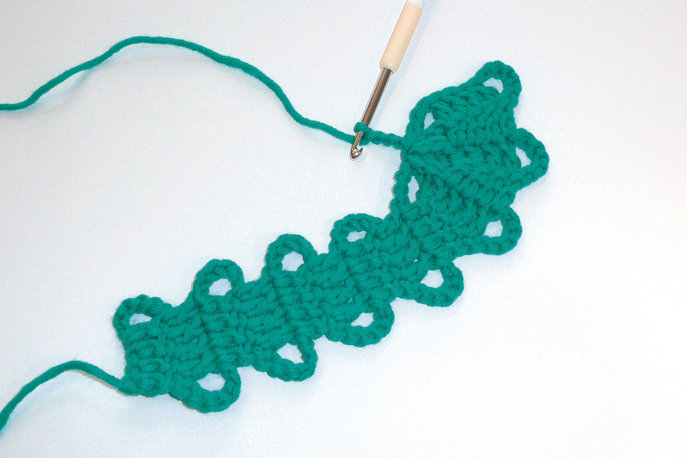 Grünes, selbstgemachtes Häkelstück; wellenförmig mit Lochmuster. Handarbeit, DIY, lebendige Farbe.