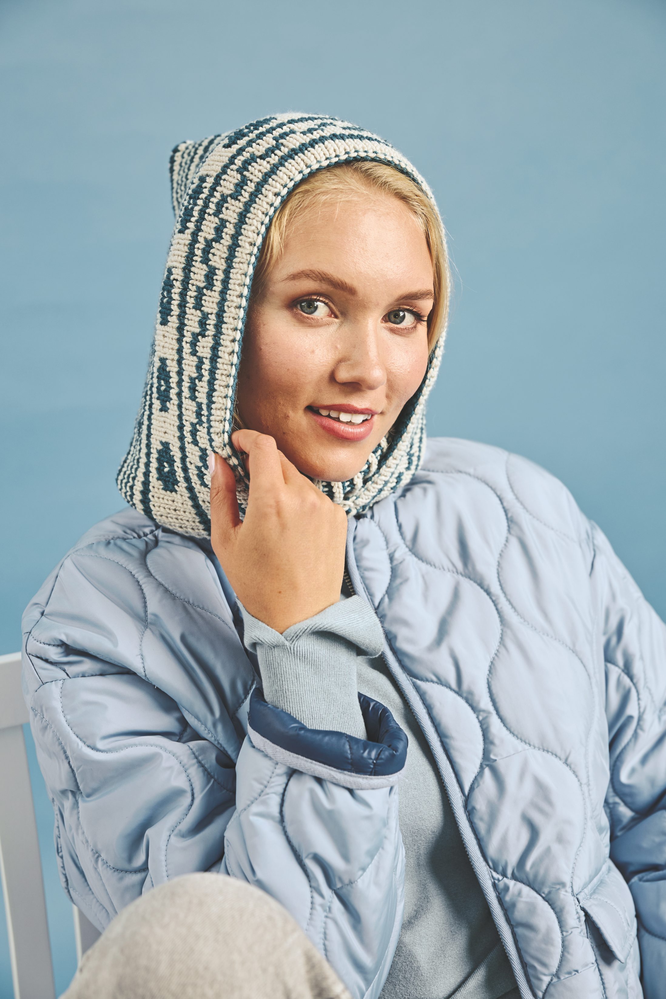 Handgemachte, gemusterte Strickhaube kombiniert mit modisch gesteppter, hellblauer Jacke.