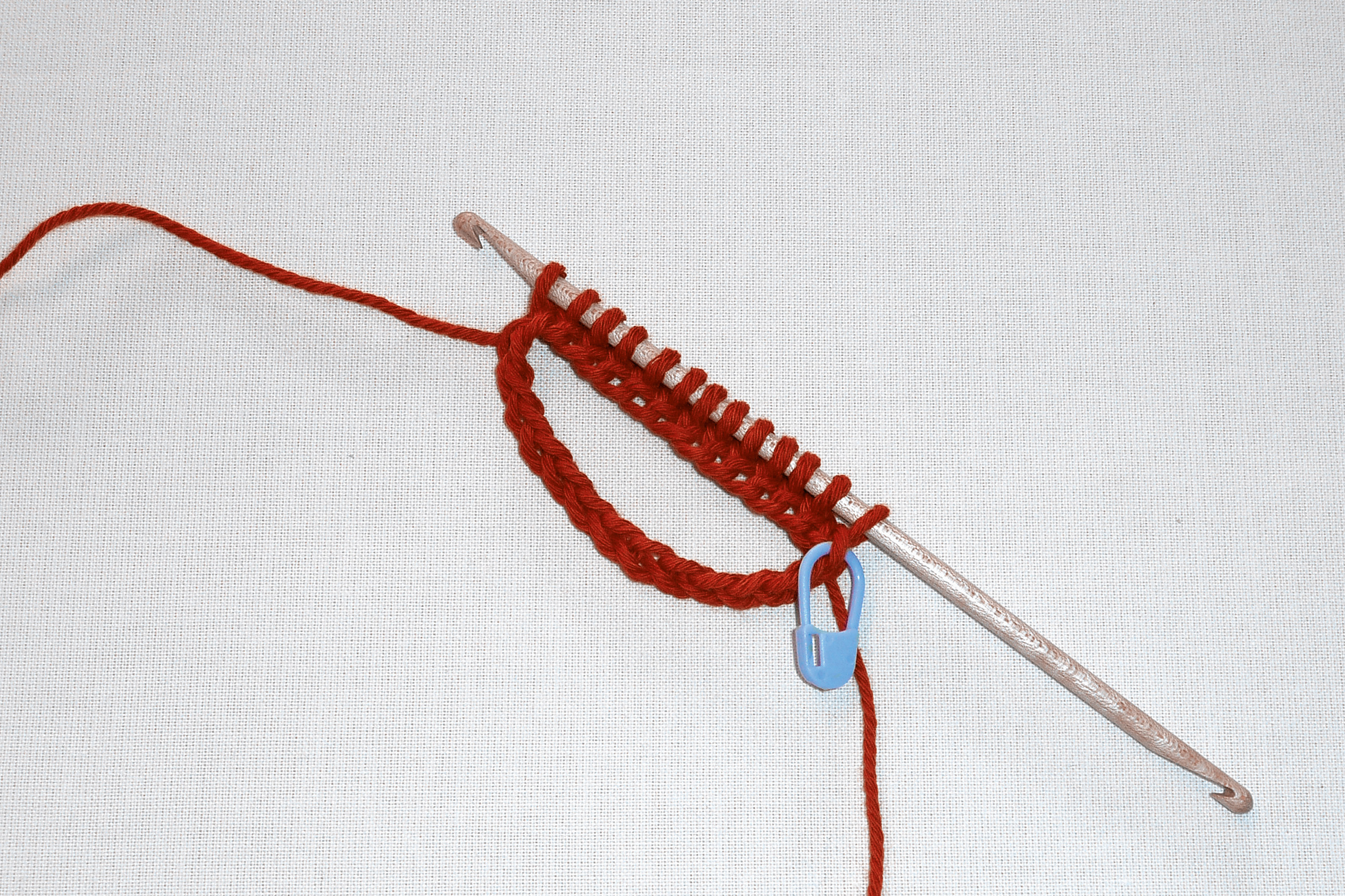 Rote Wolle auf Häkelnadel mit Maschenmarkierer, handgemacht, DIY, kreative Handarbeit.