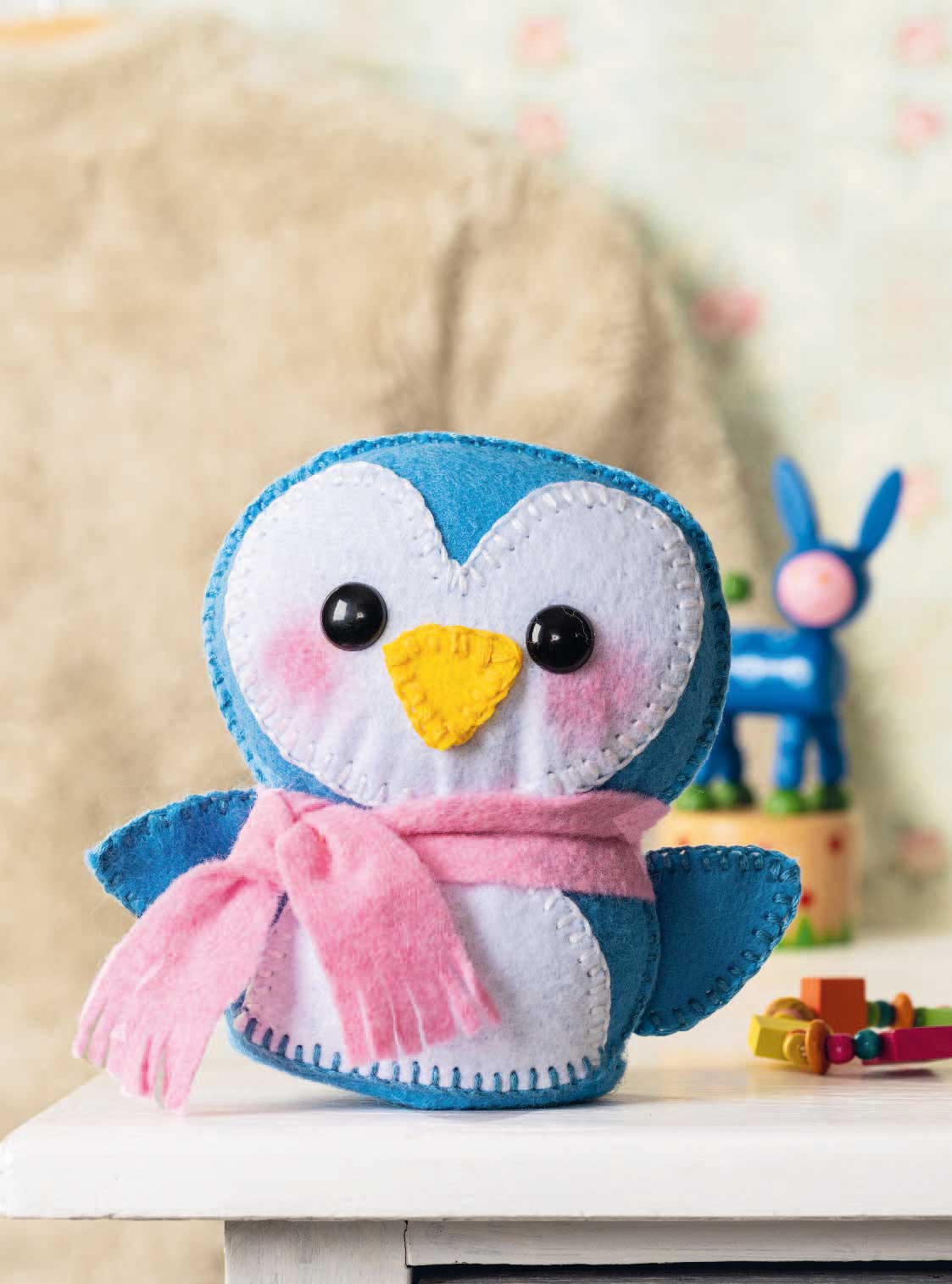 Niedlicher handgemachter Pinguin aus Filz, blau-weißer Körper, rosafarbener Schal, kreative Handarbeit.