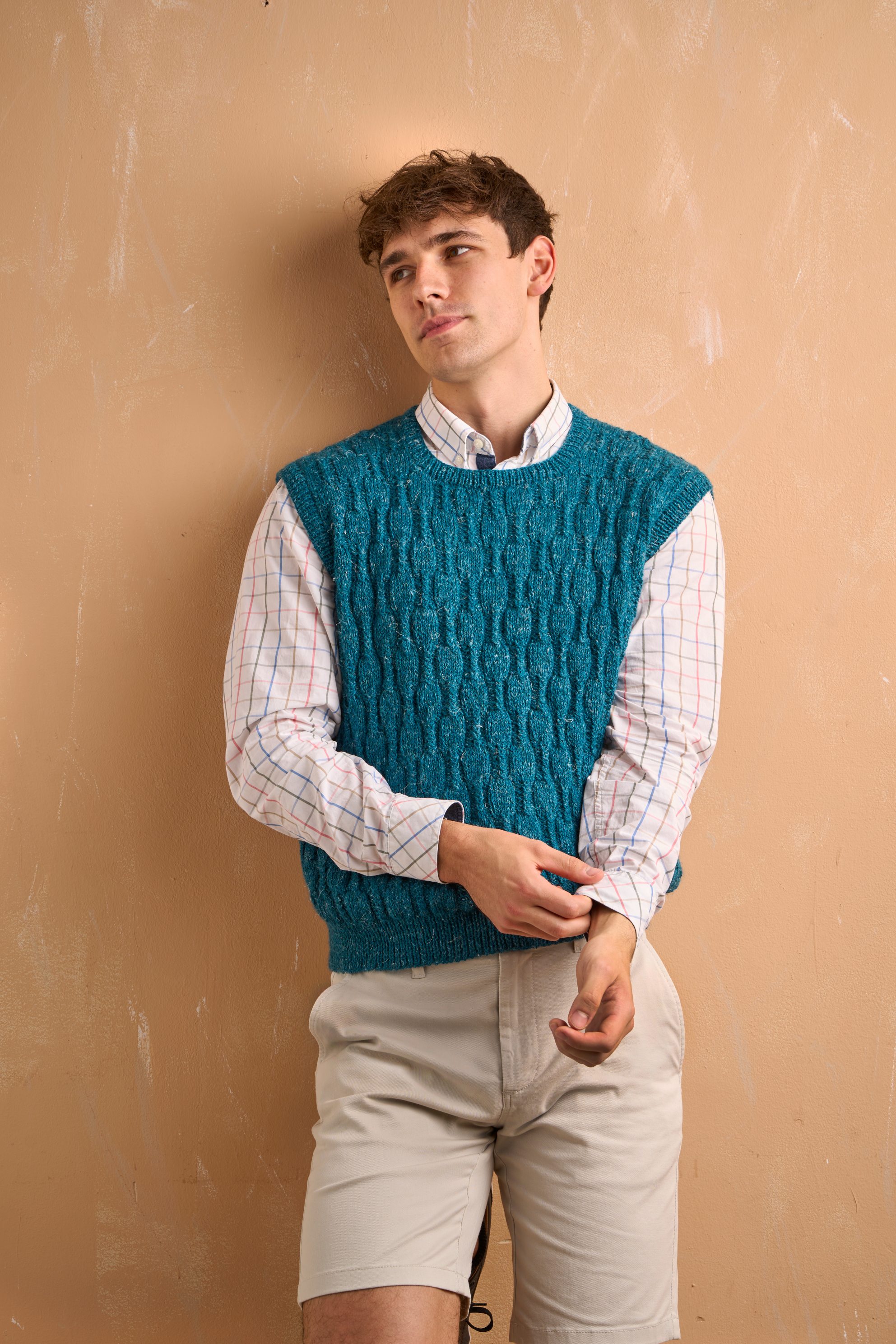 Modisch gestrickte, blaue Weste, kombiniert mit kariertem Hemd und hellen Shorts. Handarbeits-Chic.