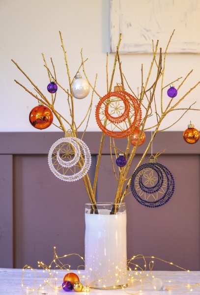 Bunte Baumschmuckstücke an goldenen Ästen, handgemachte Traumfänger in Orange, Weiß, Lila.