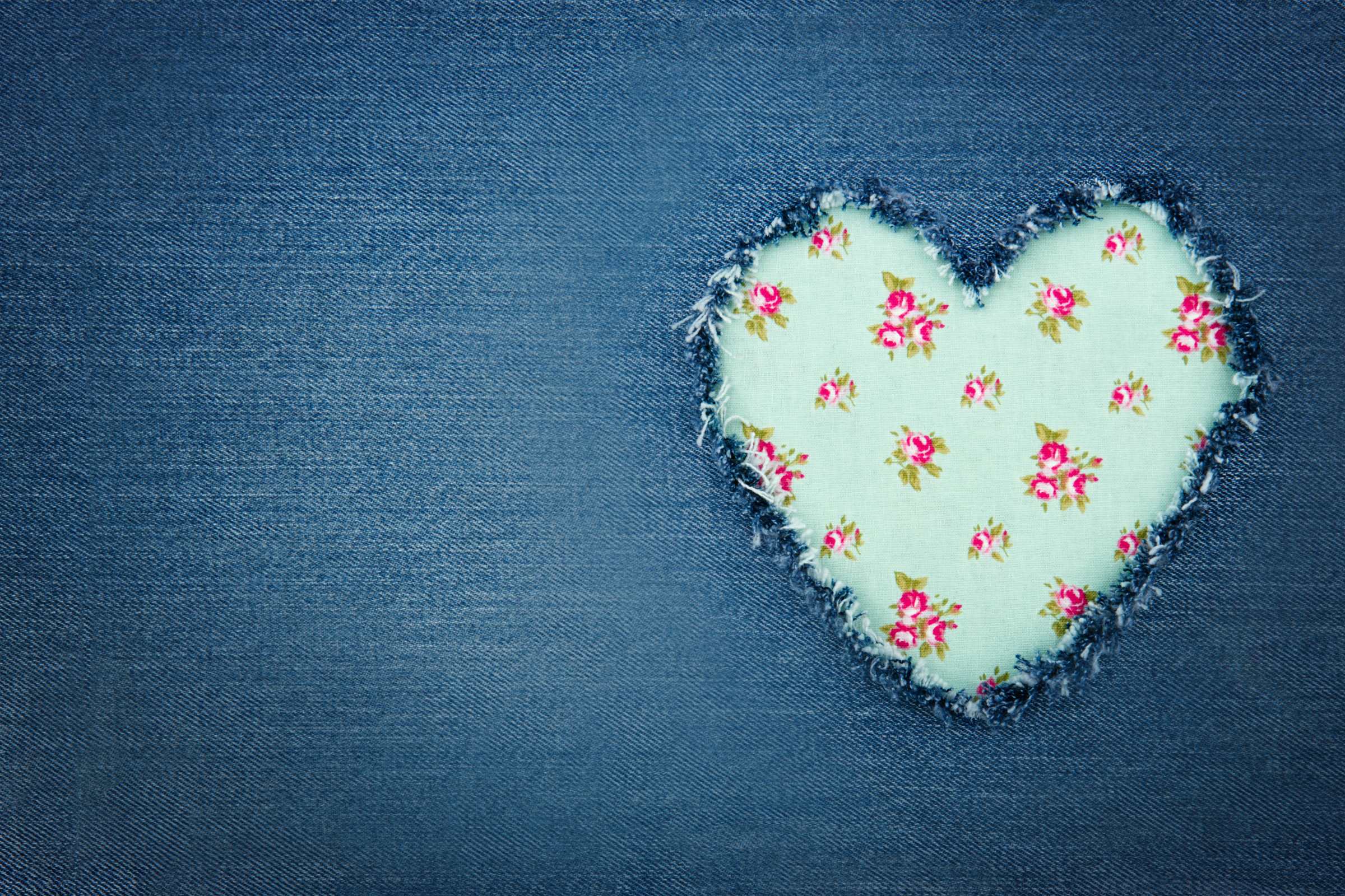 Denim mit herzförmigem Stoffpatch; florales Muster, zerrissene Kanten, handgefertigter DIY-Look, modisch.