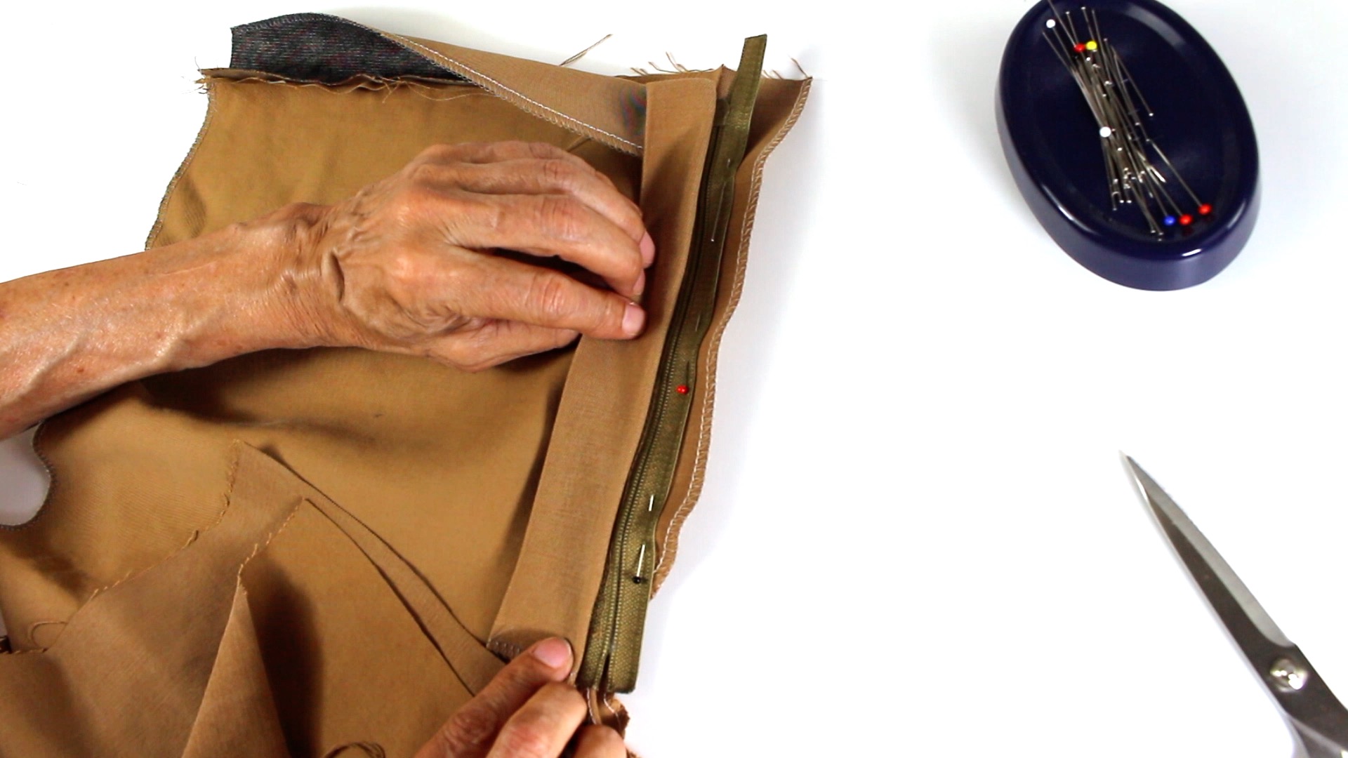 Beige Stoff, grüner Reißverschluss; Handgenäht, selbstgemacht, DIY. Präzise Handarbeit mit Nadel und Faden.