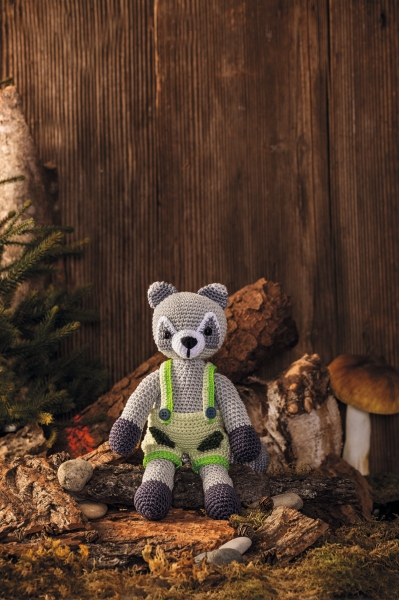 Grau-grün gehäkeltes Stofftier in Latzhose, DIY, handgemachte Details, akzentuierte Farbgebung.