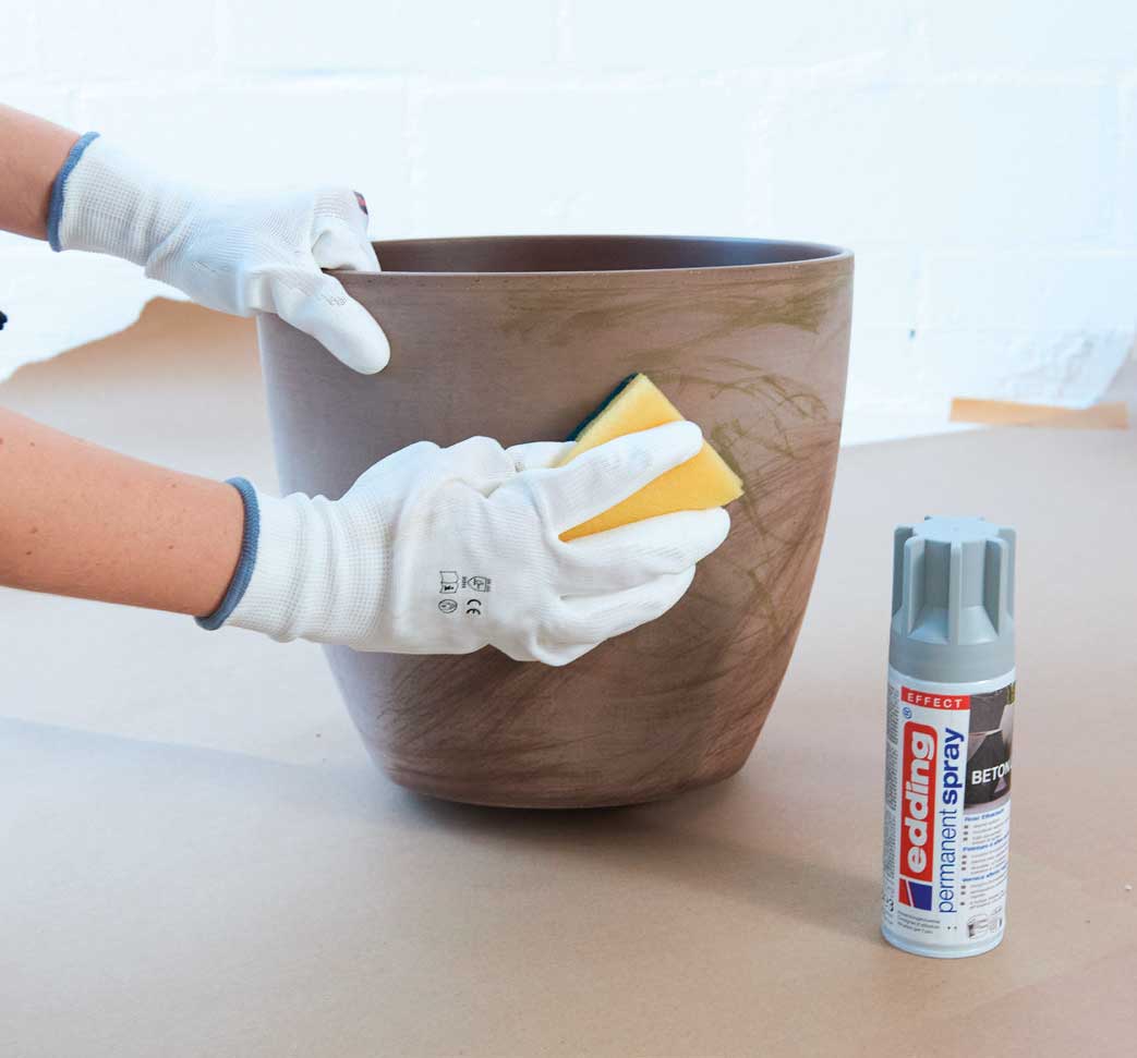 Kreatives DIY-Projekt: Topf mit Struktur, weiße Handschuhe, Schwamm und Sprühfarbe für individuellen Look.