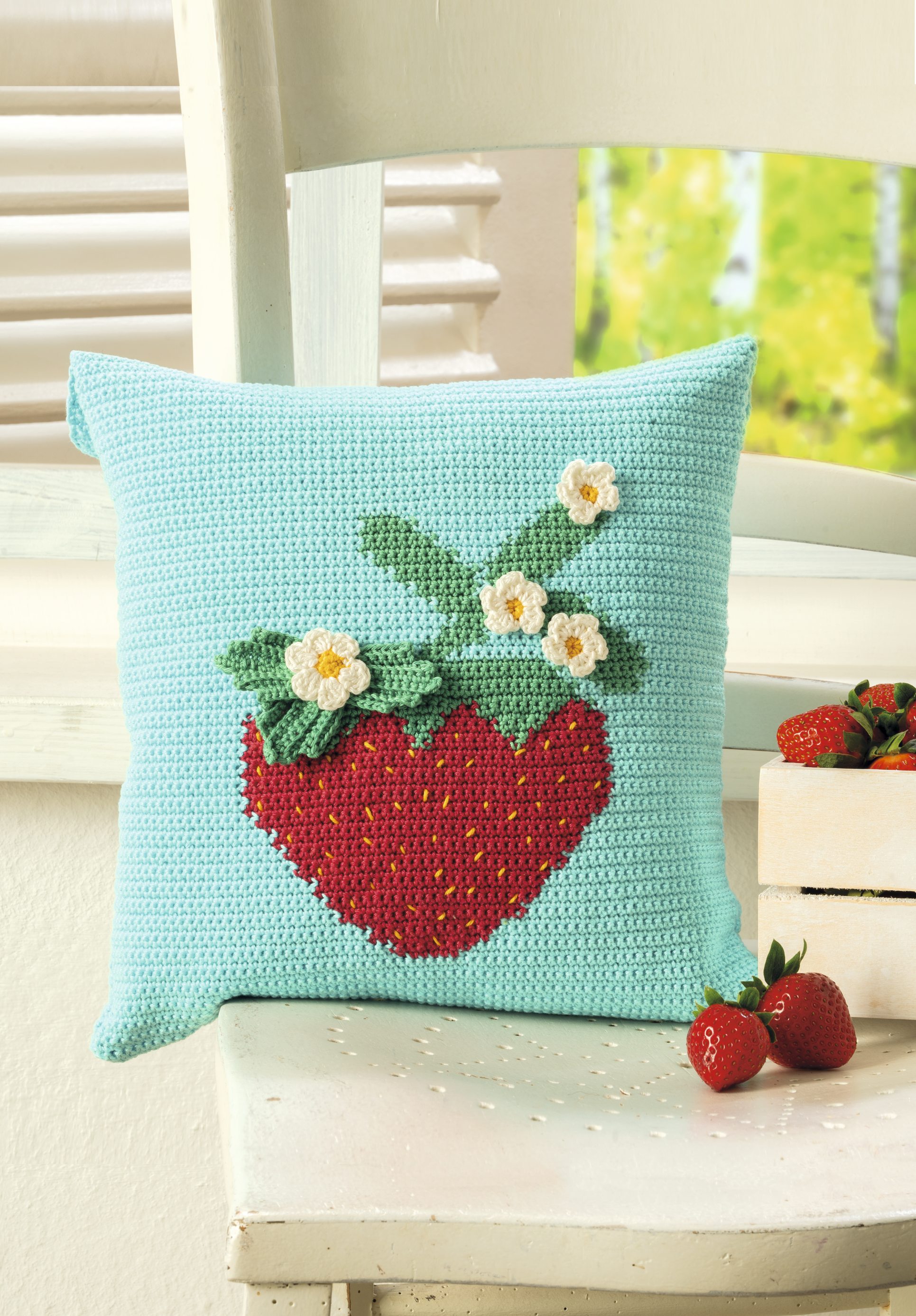 Handgemachtes Kissen in Pastellblau mit gestricktem Erdbeer-Muster. Florale Details, modisch und dekorativ.