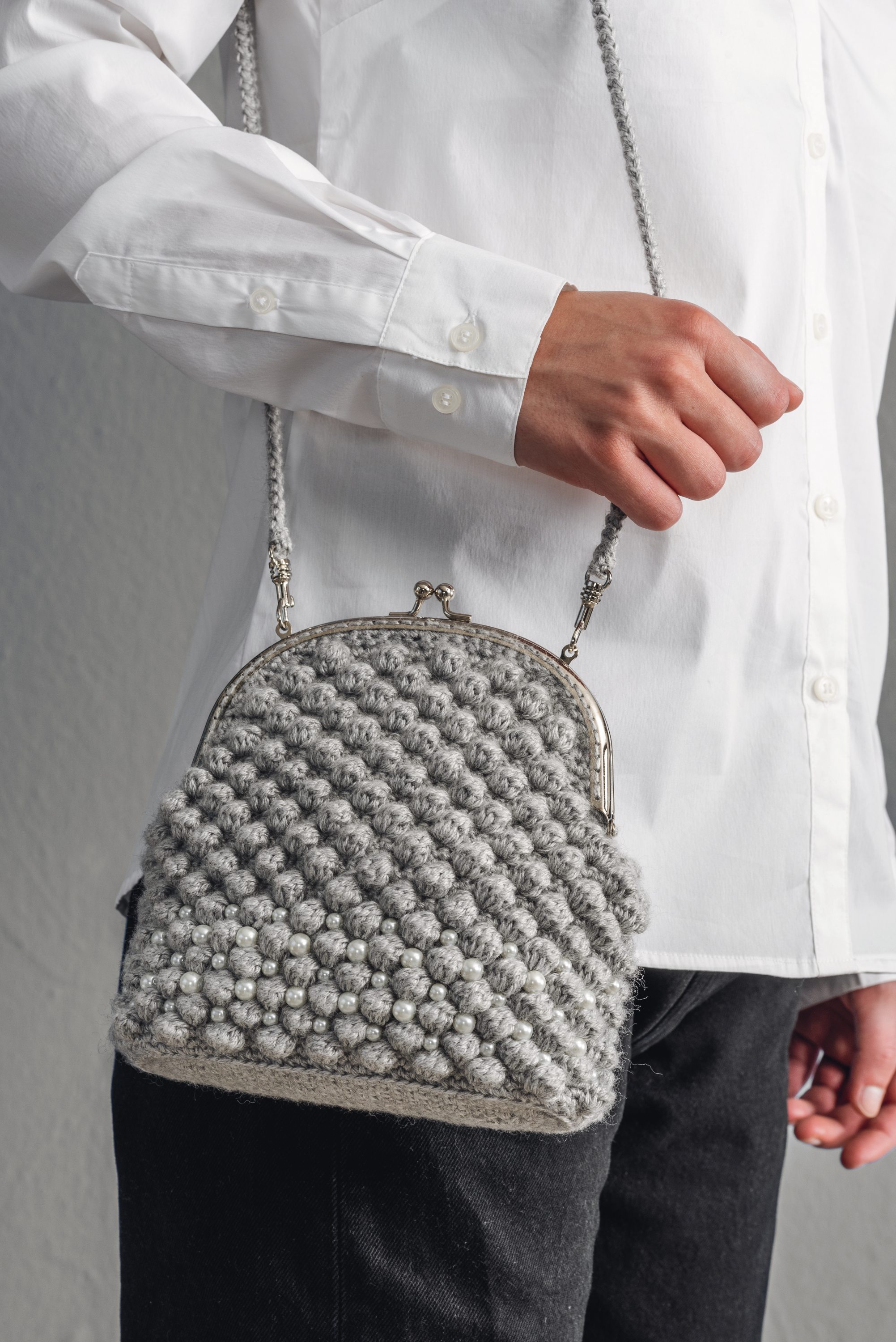 Graue, gehäkelte Tasche mit kugeligem Muster. DIY-Stil, perfekt zu schlichter, weißer Bluse und schwarzen Hosen.