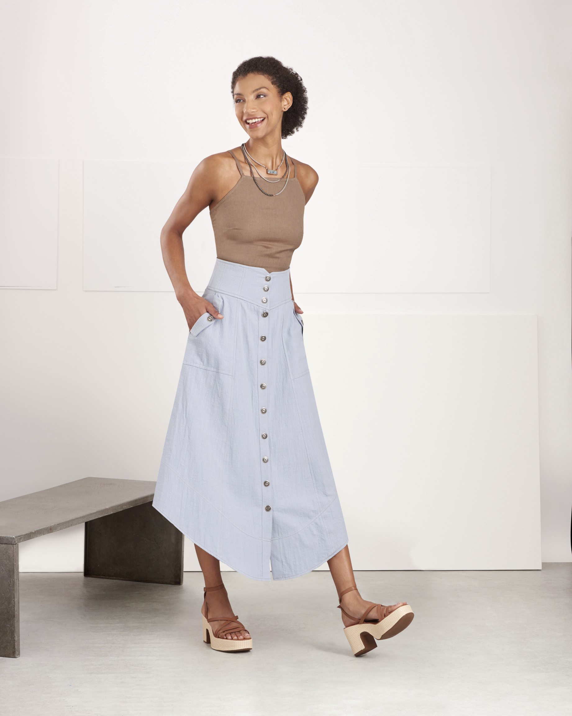 Damen in beige Top und blauem, knopfbesetztem Midirock. Schlichte Schnitte, modisch und charmant.