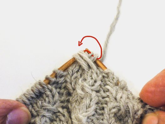 Handgemachtes Strickmuster in Beige mit komplexem Zopfdesign auf Holzstricknadeln.