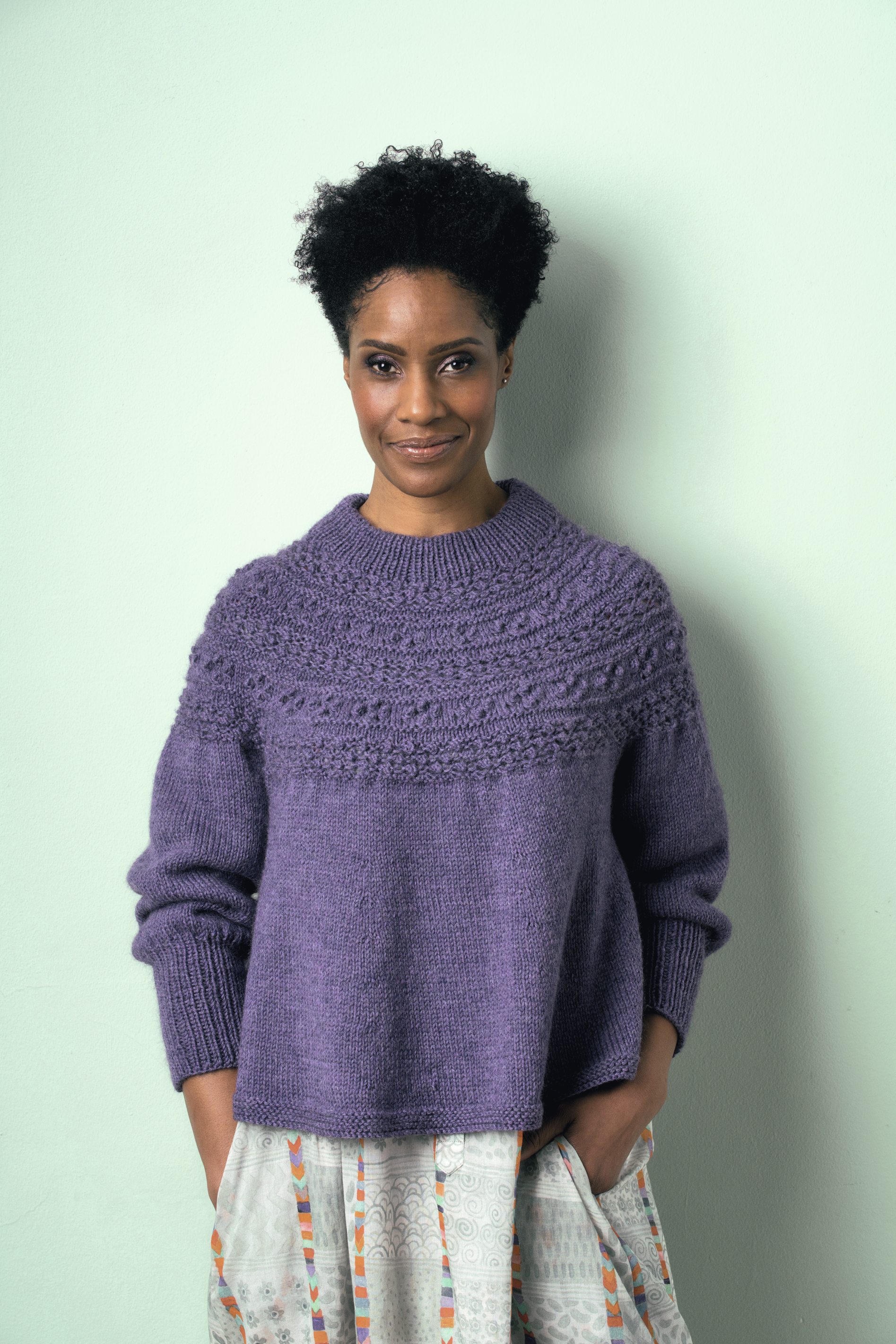 Handgemachter, lila Pullover mit schlichter Struktur und Rundhalsausschnitt, kombiniert mit gemustertem Rock.