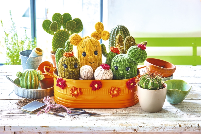 Bunte, modische Häkelkakteen in Gelb und Grün mit niedlichen Gesichtszügen und Blüten. Kreative Handarbeit, DIY-Style.