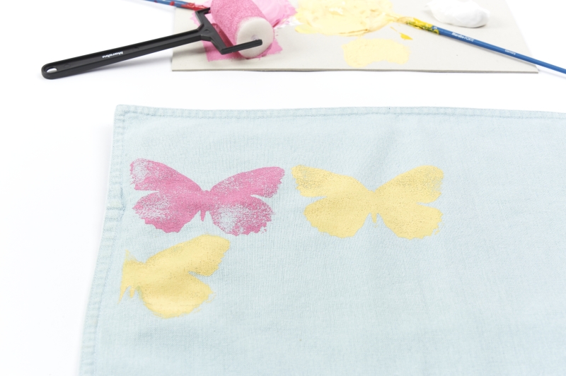 Hellblauer Stoff mit pinken und gelben Schmetterlingsmustern, handgemalt. Modisches DIY-Muster.