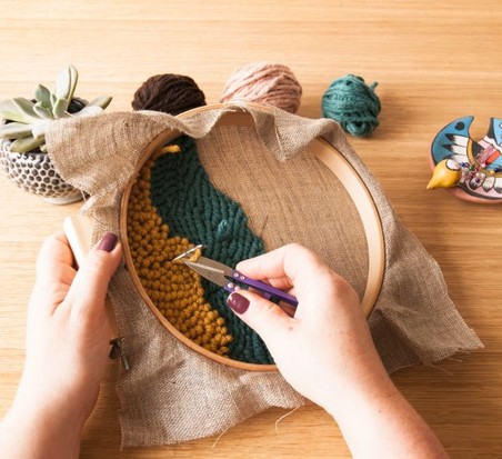 Farbige Wollmuster in Grün und Gelb auf beigem Stoffring. DIY-Handarbeit.