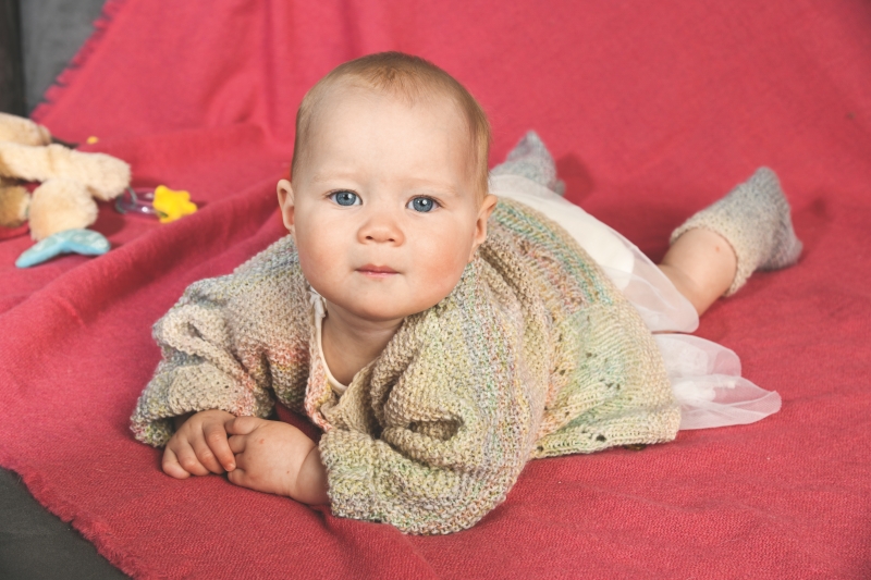 Handgestrickter Cardigan in sanften Pastelltönen, kombiniert mit weißen Söckchen. DIY-Chic für Babys.