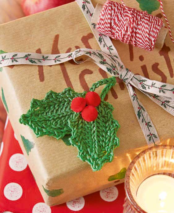 Handgemachtes, gestricktes grünes Blatt mit roten Beeren als Verzierung auf Geschenk, modisch und kreativ.