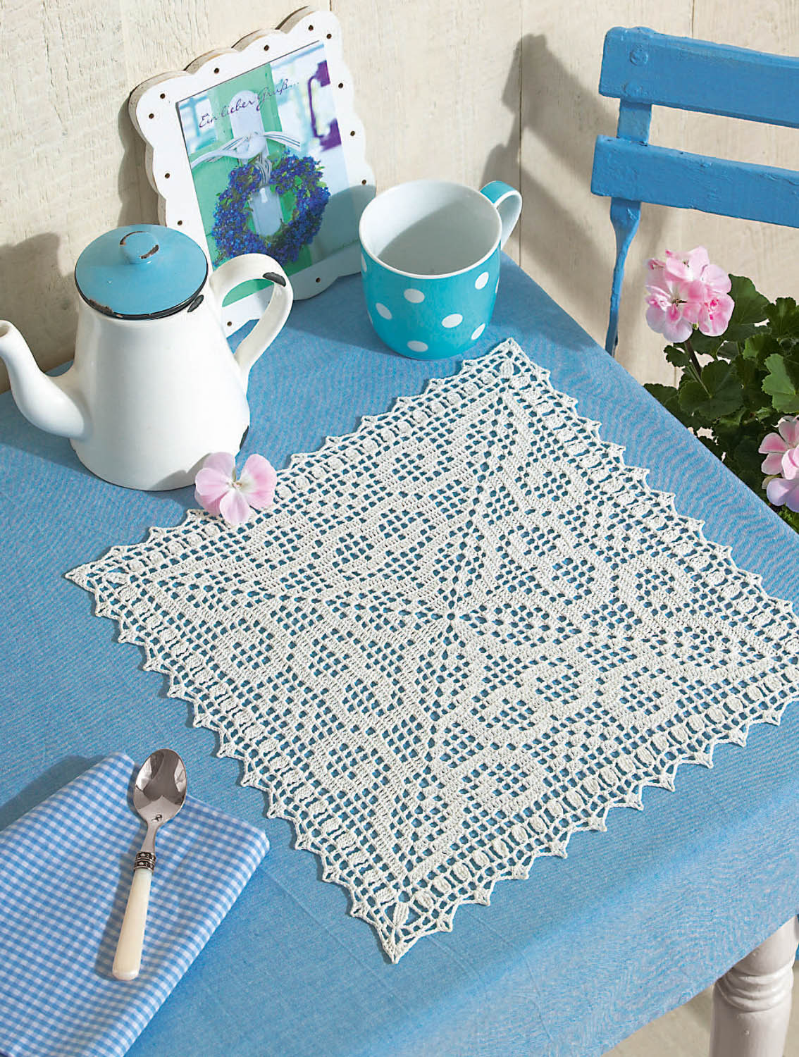 Weißes, handgemachtes Häkelmuster auf blauem Stoff, elegant und filigran, ideal für DIY-Dekoration.