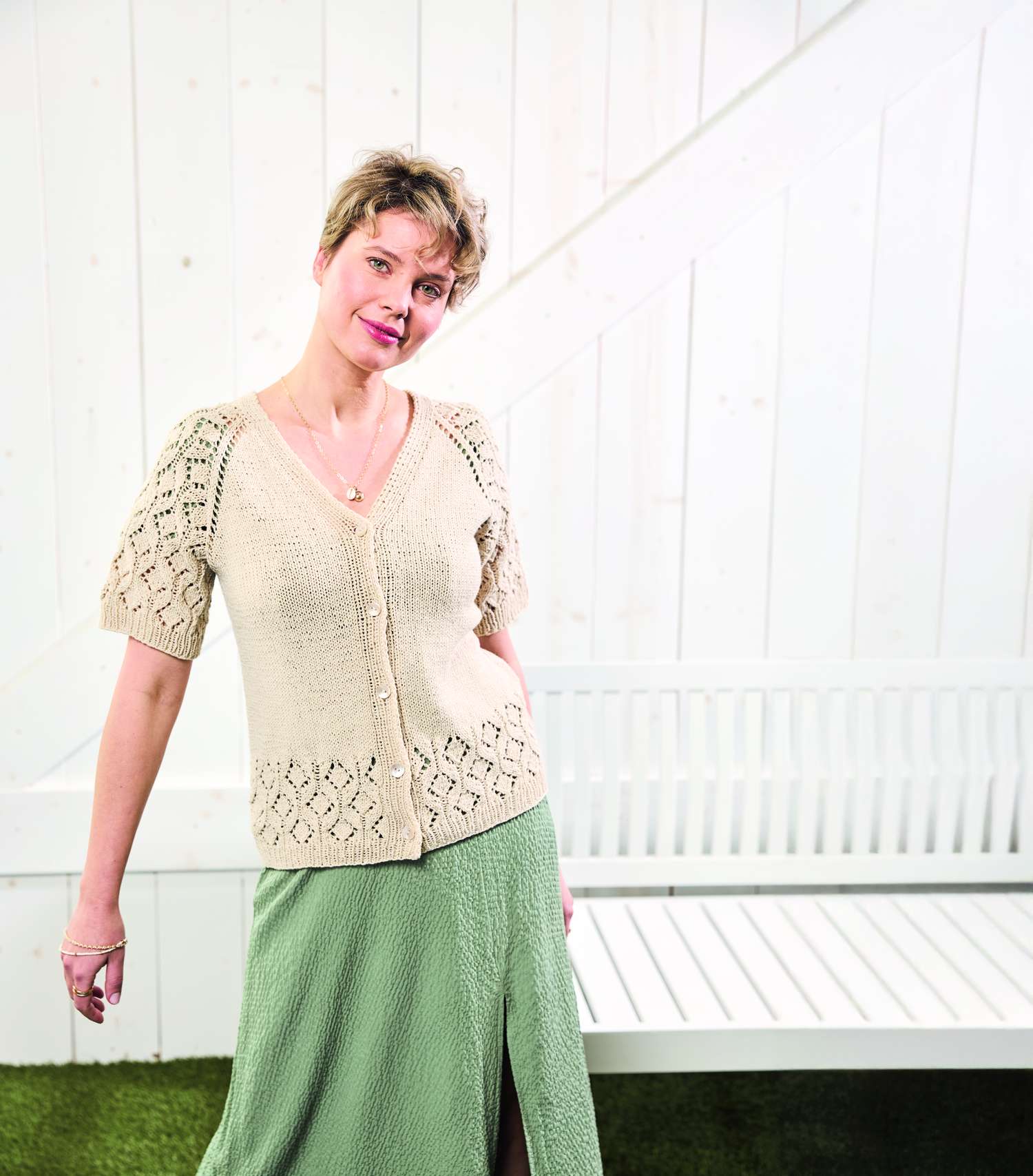 Beigefarbener Strick-Cardigan mit Lochmuster, kombiniert mit einem grünen Rock in fließendem Schnitt. Modisch, elegant.