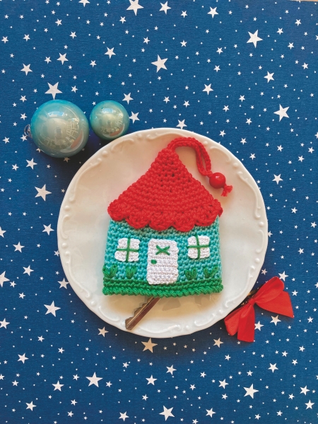Buntes DIY-Häuschen aus Garn, mit rotem Dach und grünen Wänden, kunstvoll gehäkelt. Handarbeit, einzigartig.