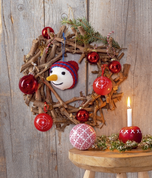 Rustikaler, handgemachter Kranz aus Zweigen mit roten Kugeln und gestricktem Schneemann für festlichen Flair.