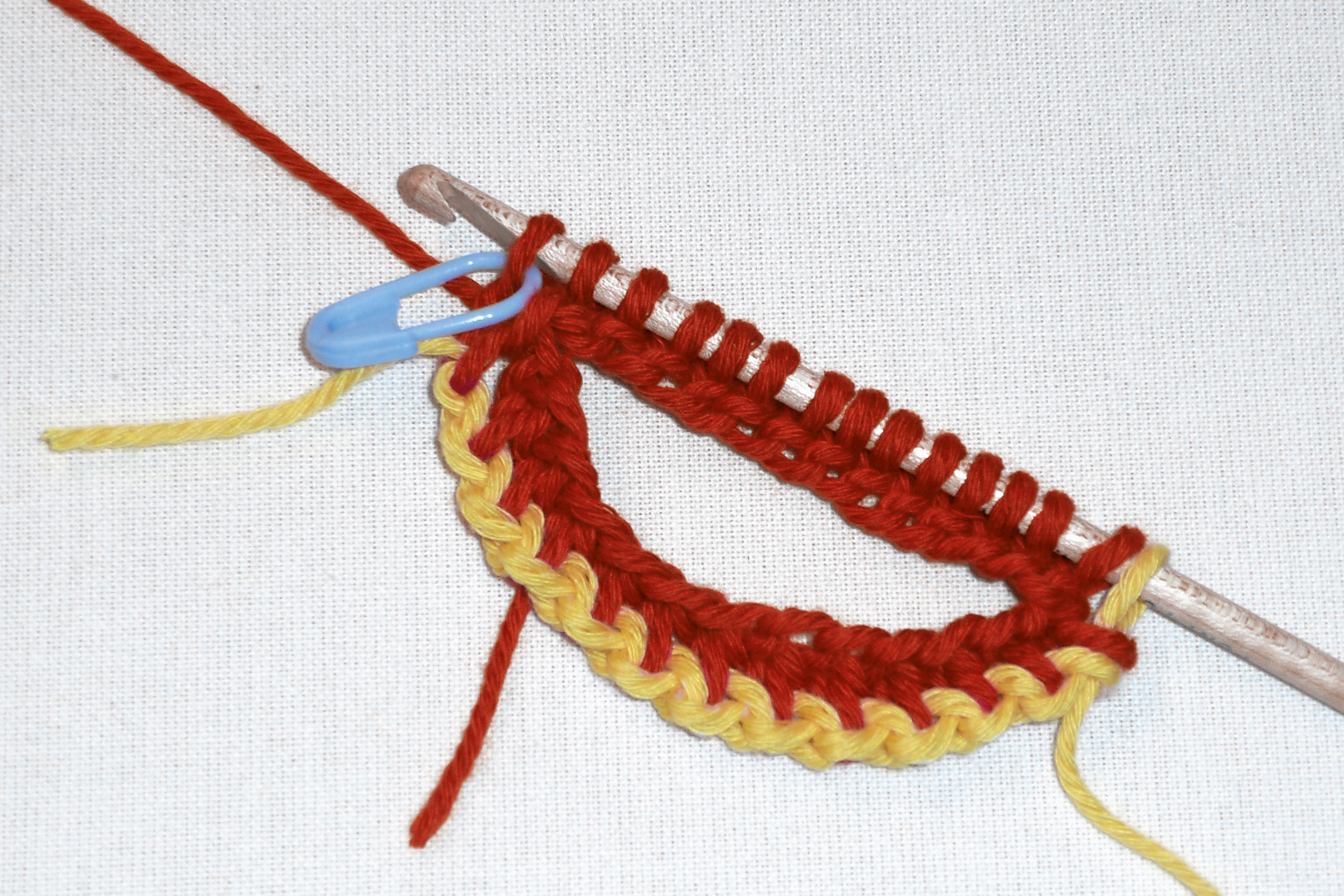 Zweifarbig, gelb-rote Wolle, handgemacht, Detailansicht. DIY-Stil, mit Häkelnadel und Maschenmarkierer.