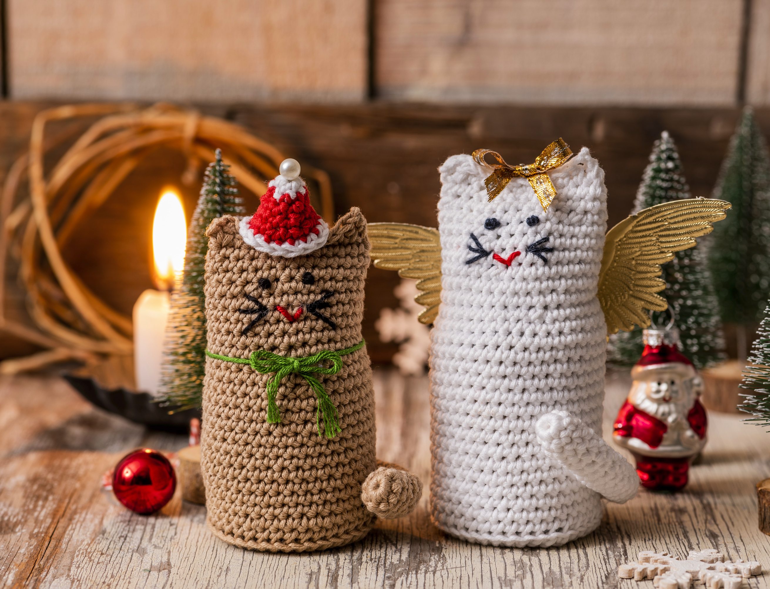 Zwei handgemachte Häkelkatzen, eine in Braun mit roter Mütze, die andere in Weiß mit goldenen Flügeln. DIY-Charme.