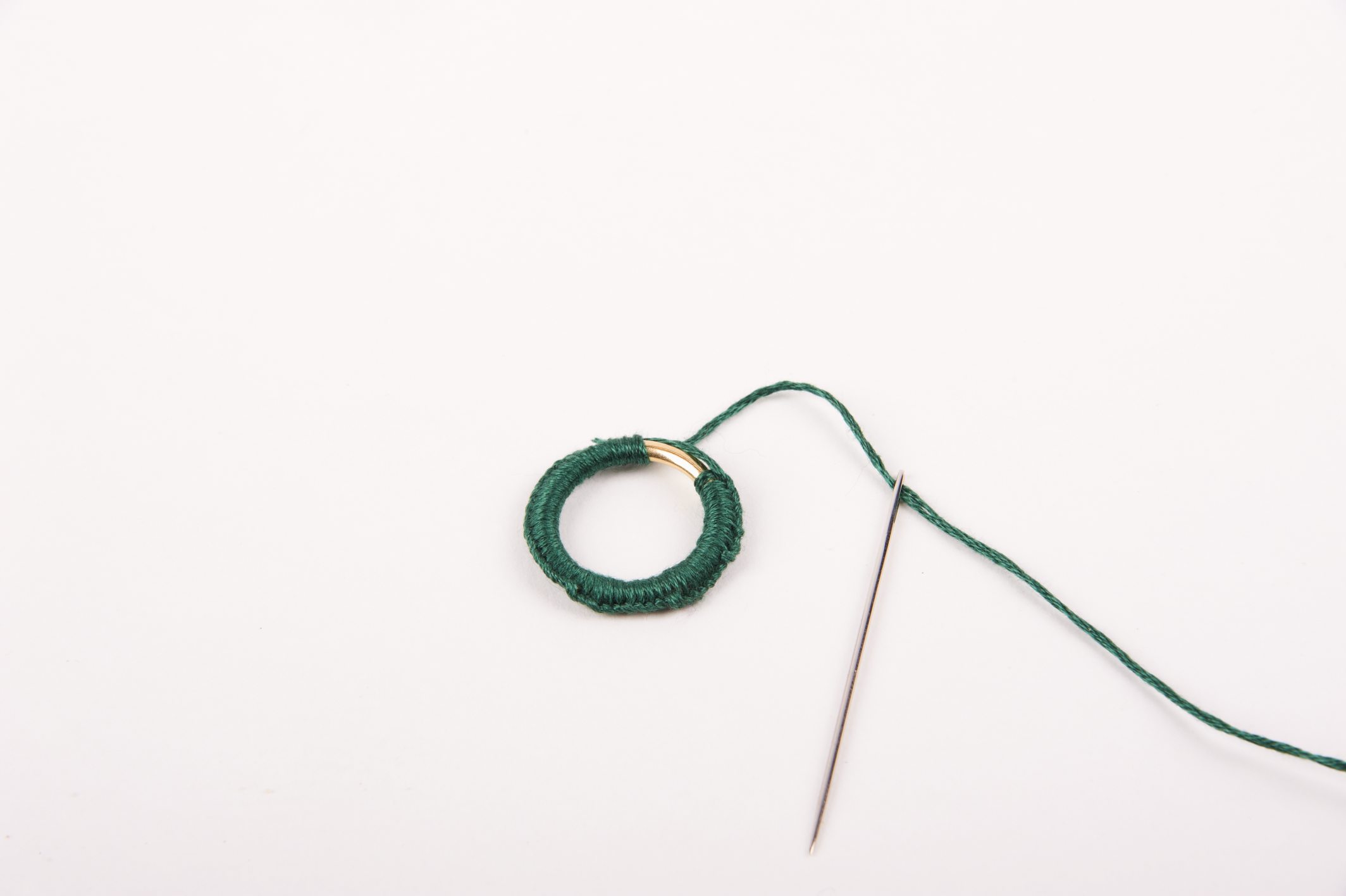 Grüner Faden um Metallring gewickelt mit Nadel; minimalistisch, handgemacht, modische Einfachheit.