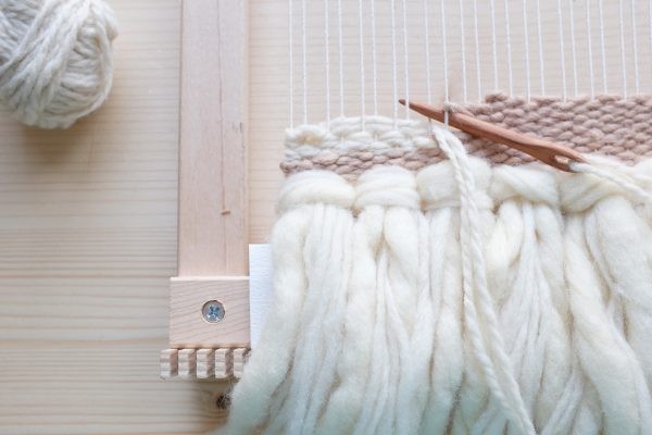 Strukturiertes, handgemachtes Gewebe in Creme- und Beigetönen mit grobem, flauschigem Garn. DIY-Kunstwerk.