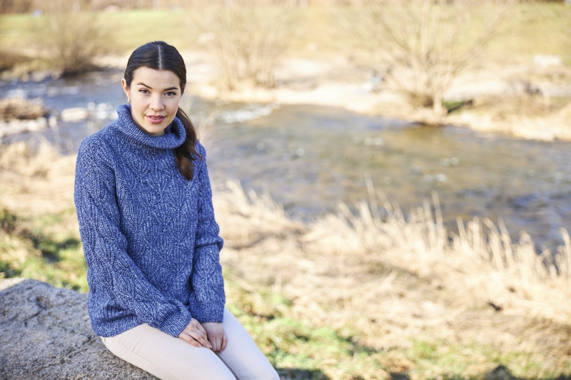 Blauer, handgemachter Zopfmusterpullover mit Rollkragen, kombiniert mit hellen Hosen. Stilvoll und gemütlich.
