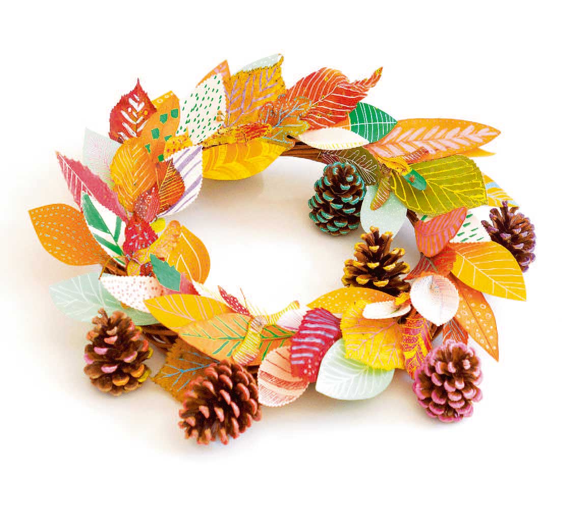 Bunter handgemachter Kranz aus Papierblättern und Tannenzapfen, herbstliche Farben und Muster. Kreative Handarbeit.