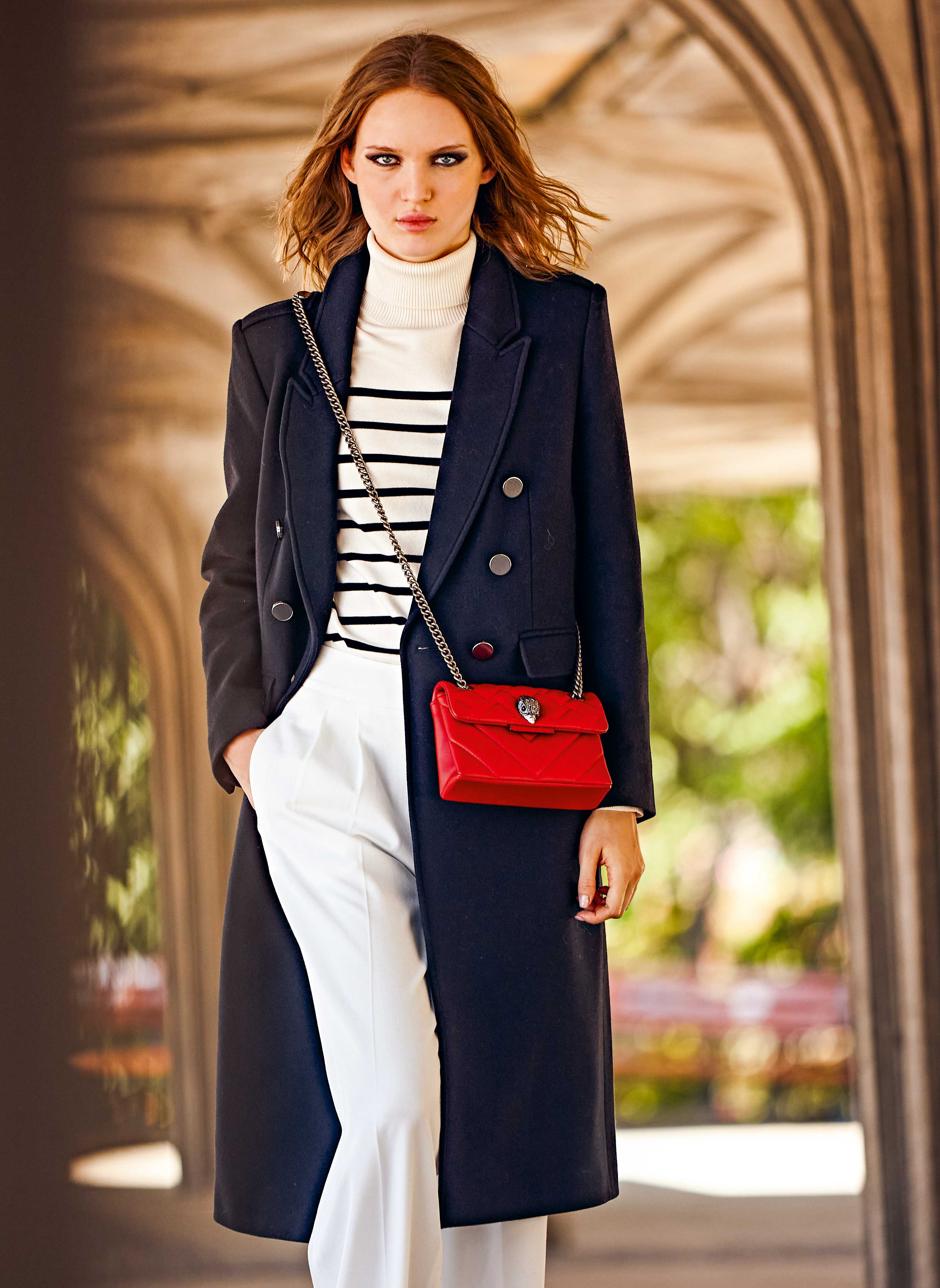 Marineblauer Mantel, Streifenpullover, weiße Hose. Akzent mit roter Tasche. Modisch und stilbewusst.