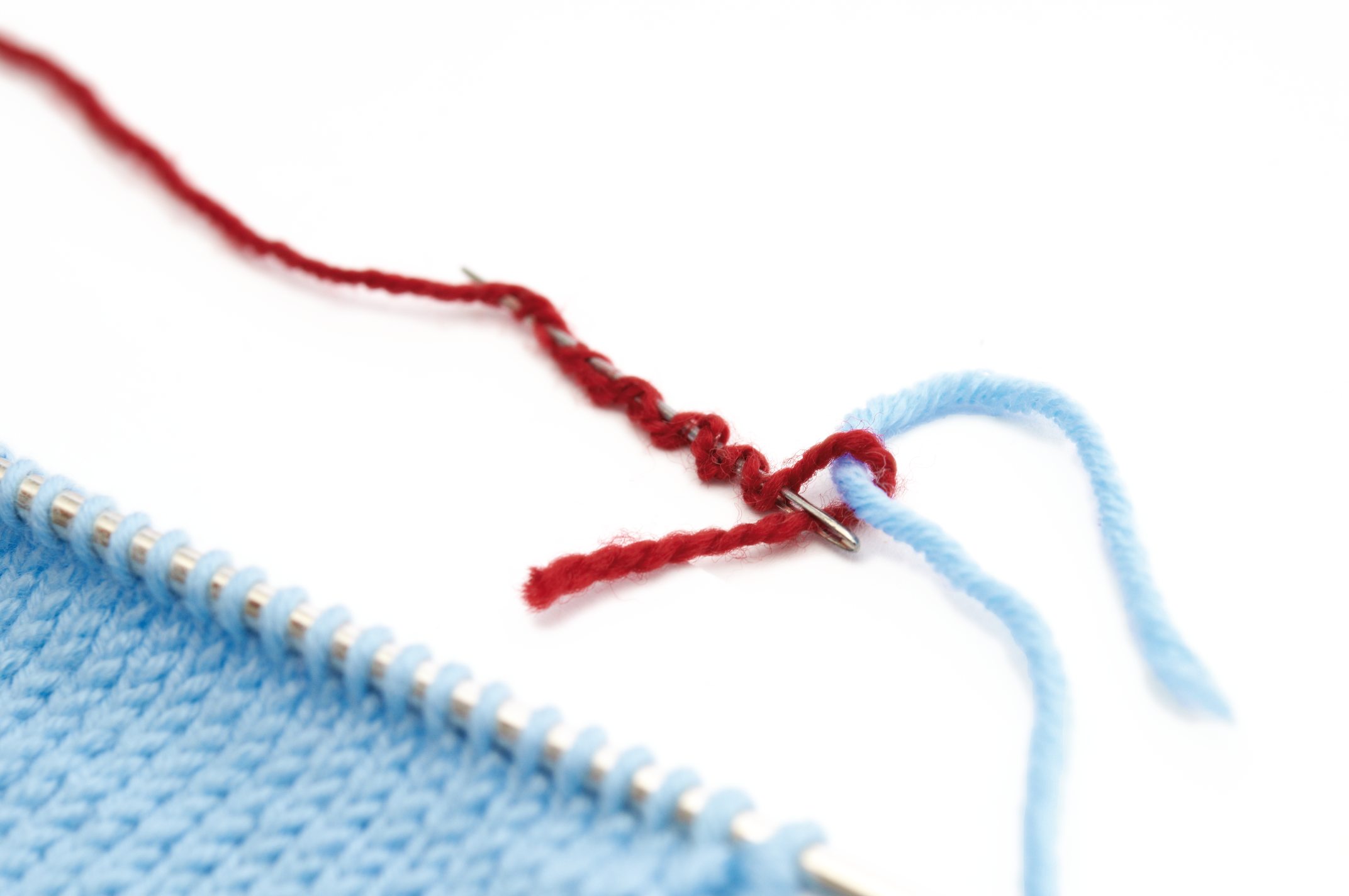 Blaue Strickarbeit auf Nadeln mit rotem Fadenansatz, handgemacht, DIY.