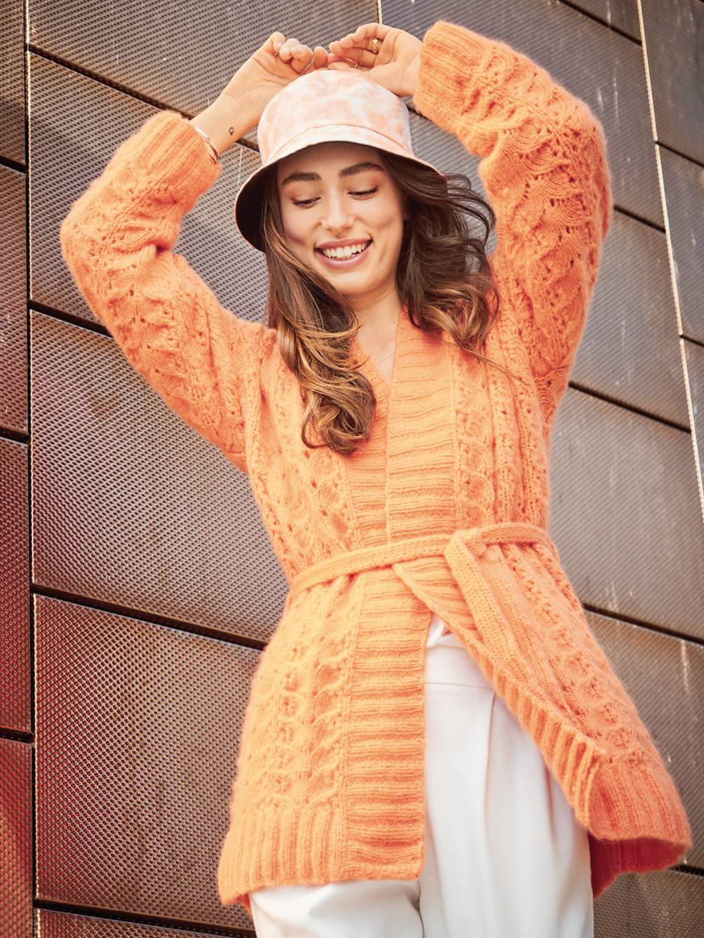 Modischer orange Strickcardigan mit Zopfmuster, Selbstgürtel und Freizeit-Bucket-Hut. Handgearbeitetes Design.