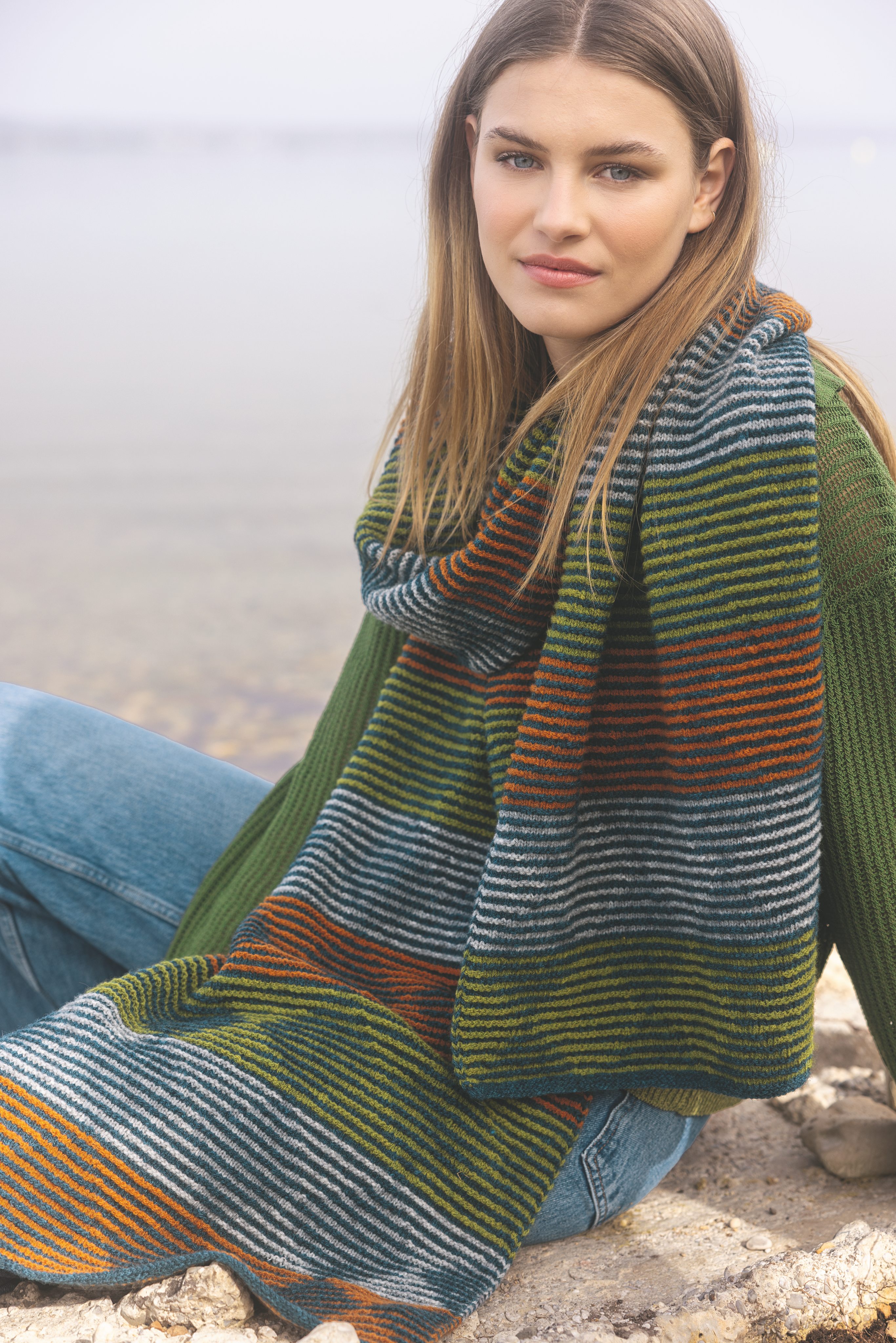 Handgestrickter Schal in Orange, Grün, Blau. Modisches Streifenmuster, lässig gewickelt, über grünem Pullover.