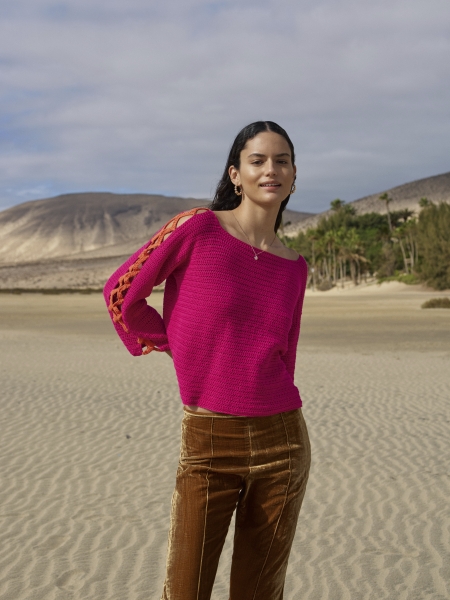 Fuchsia Strickpullover mit geflochtenem Ärmel; braune Samt-Jeans, modisch und handgefertigt, auffälliges Design.