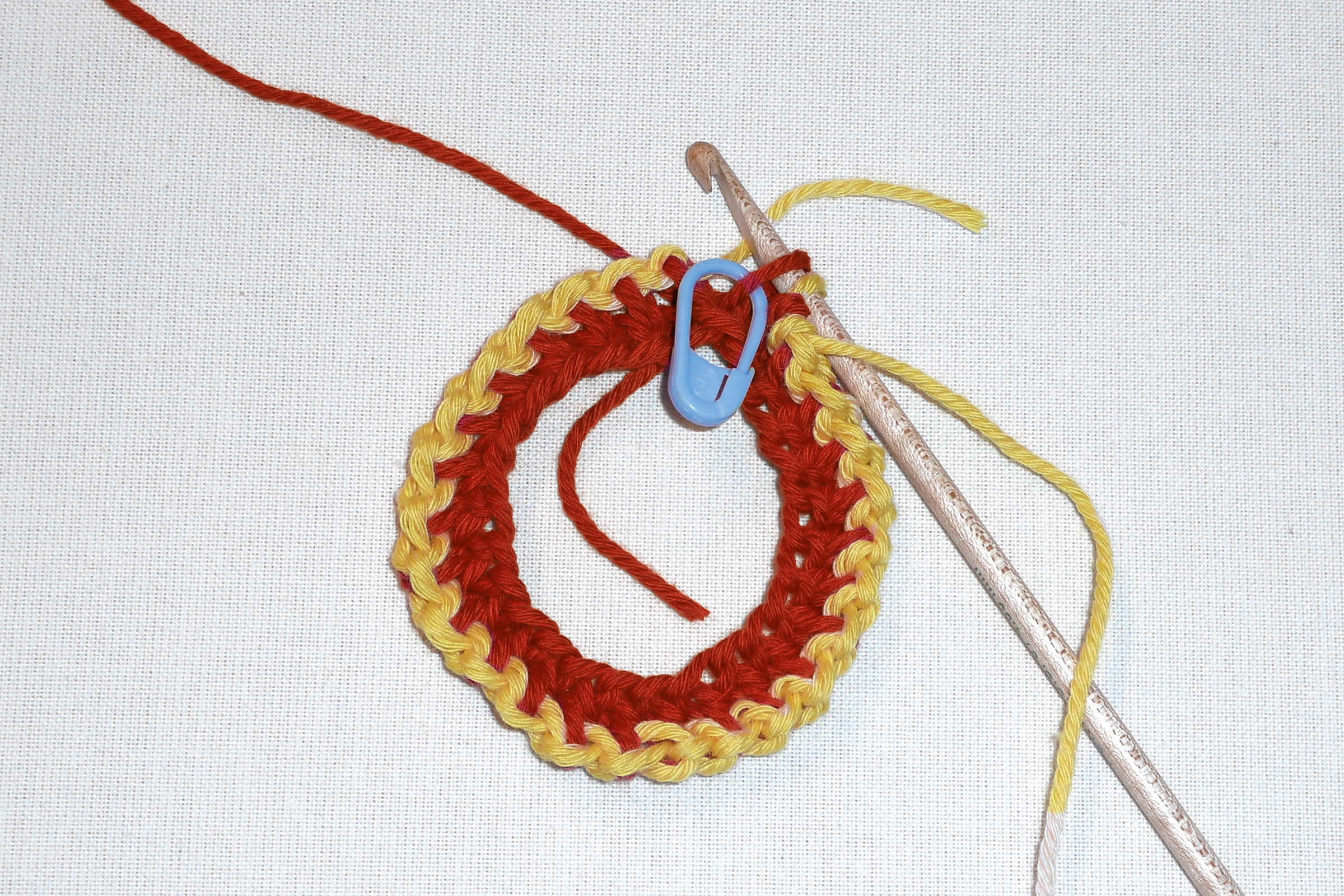Bunter Häkelring in Rot und Gelb, DIY-Handarbeit. Großer Haken und blaue Markierung.