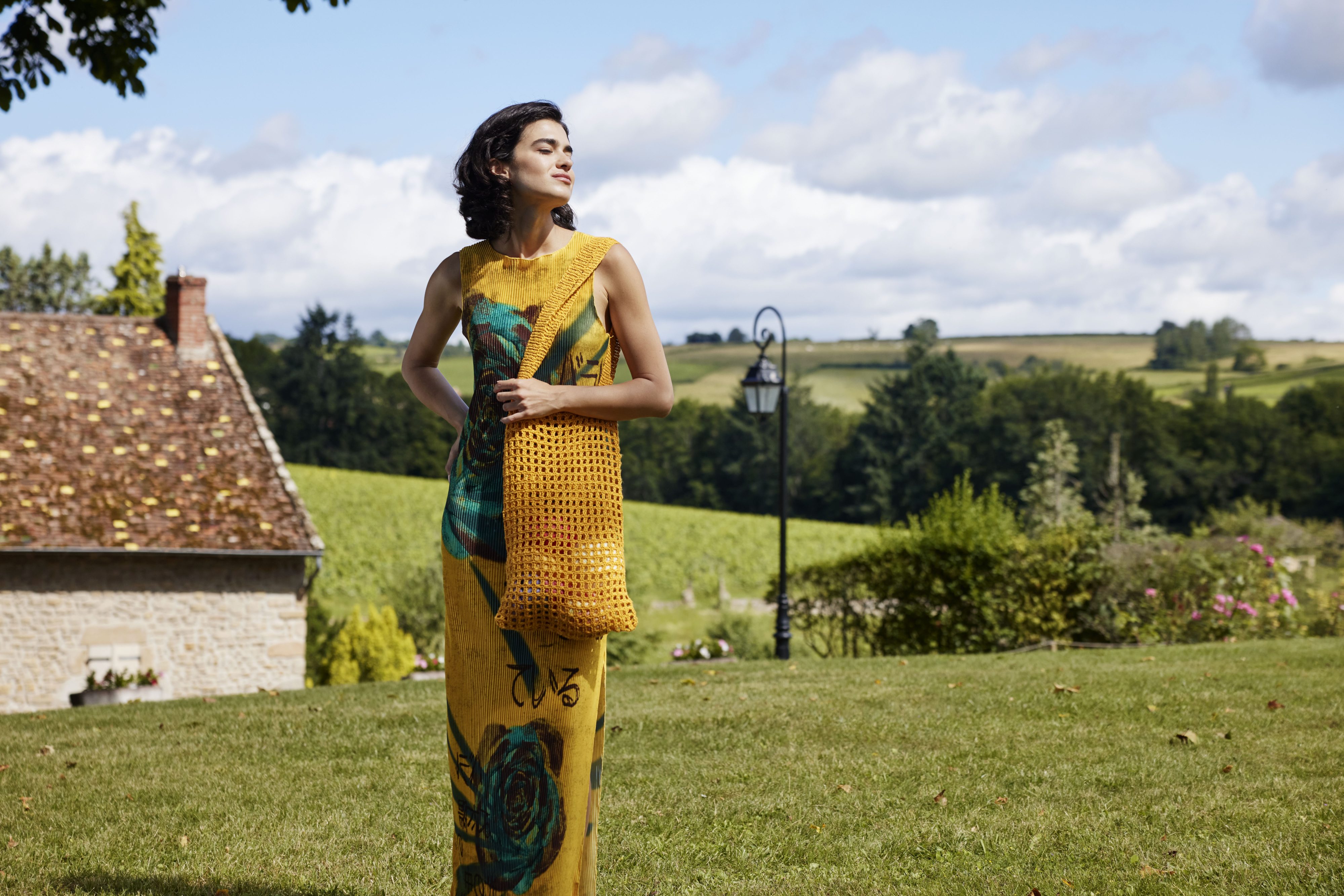 Gelbes Kleid mit Blumendruck, schlanker Schnitt. Modische handgemachte Tasche in warmen Tönen.
