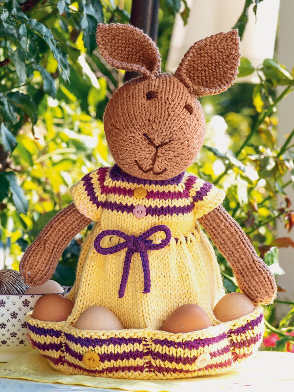 Strickhase mit gelbem Kleid, lila Streifen und Knöpfen. DIY-Charme, ideal für Kreative!