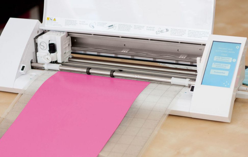 Ein Vinylschneider schneidet präzise ein leuchtend pinkes Blatt. Perfekt für handgemachte DIY-Projekte.